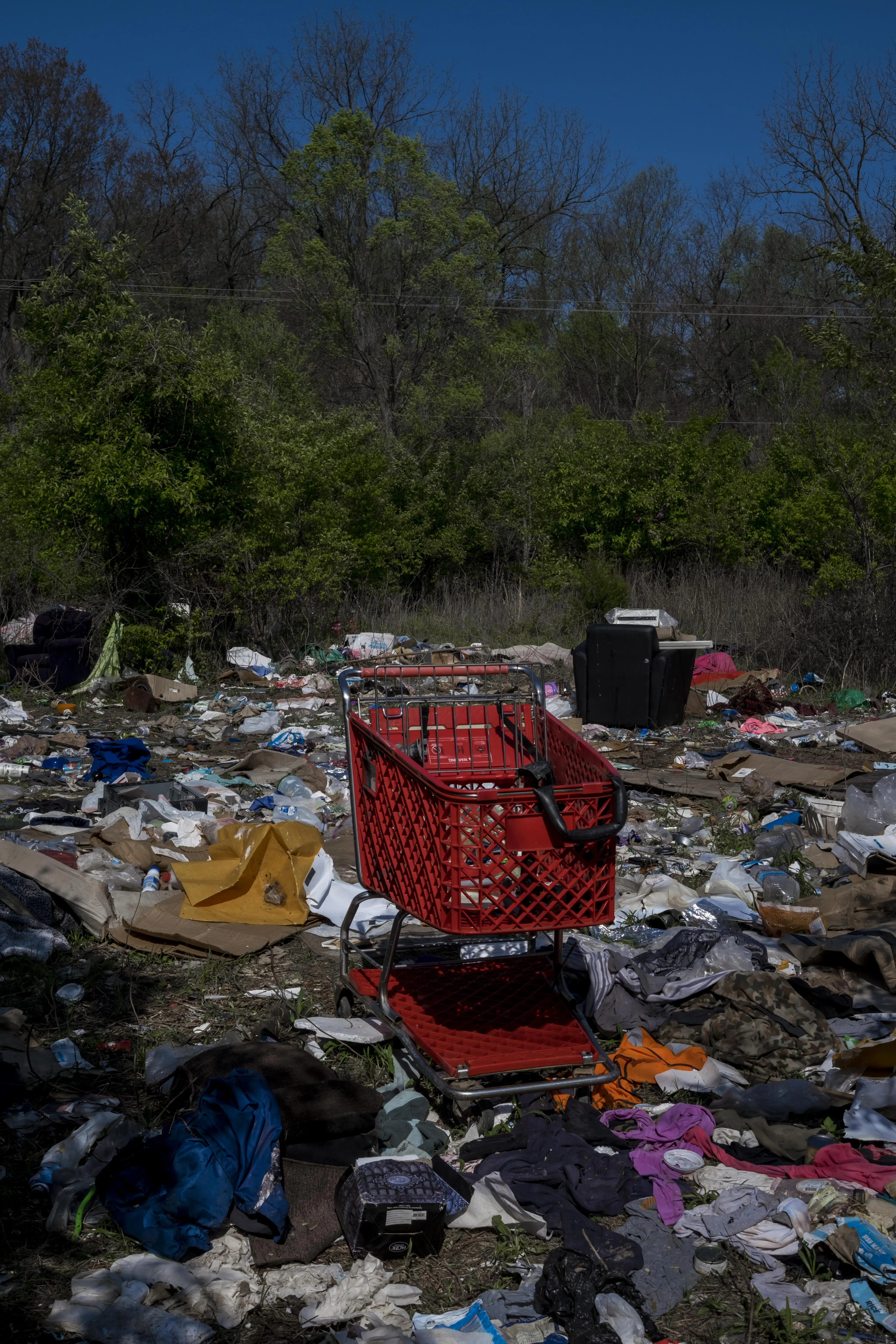 An empty shopping cart is shown outside and atop strewn clothes and debris.