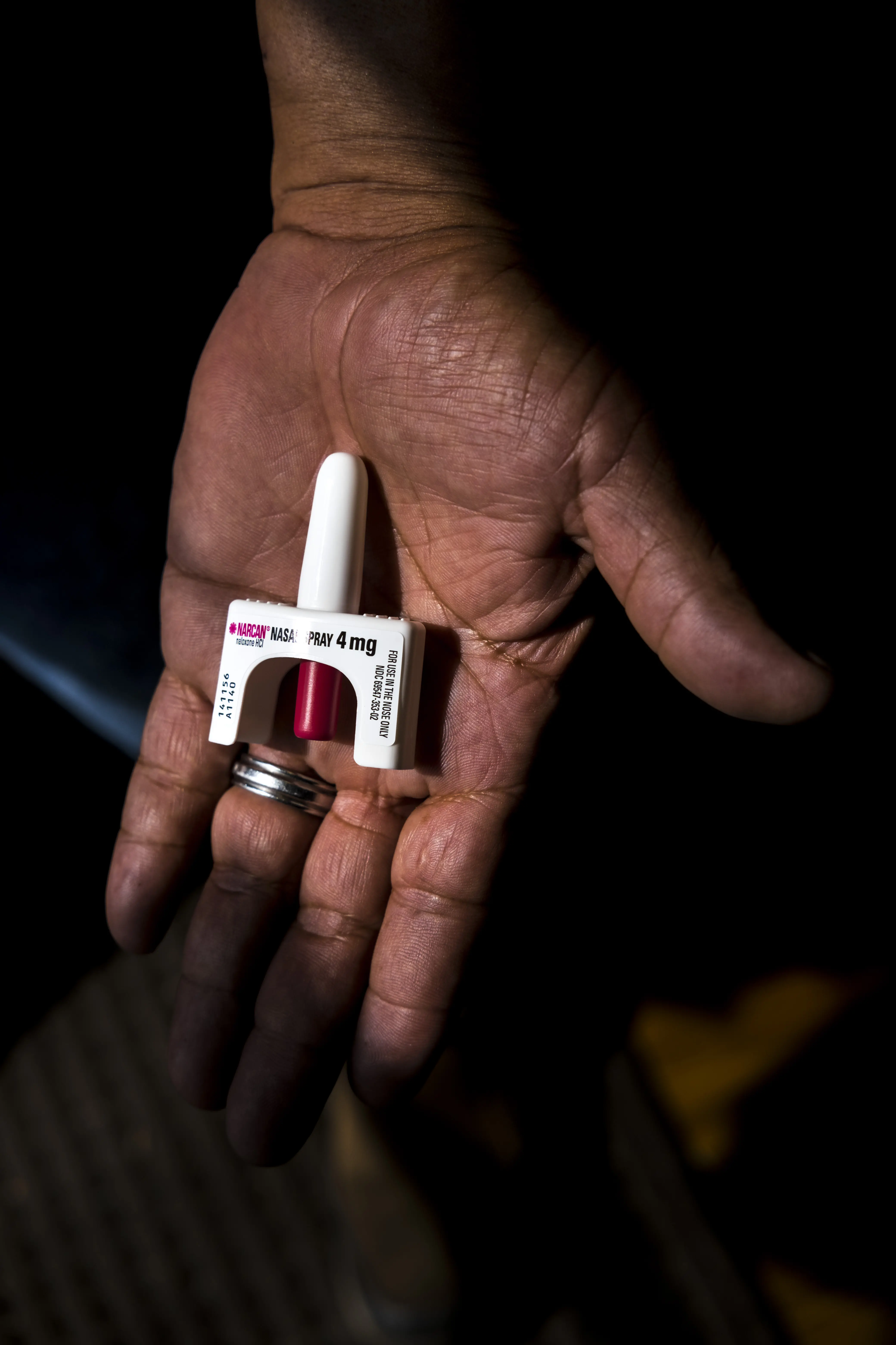 Naloxone spray in a hand glinting in a column of light.