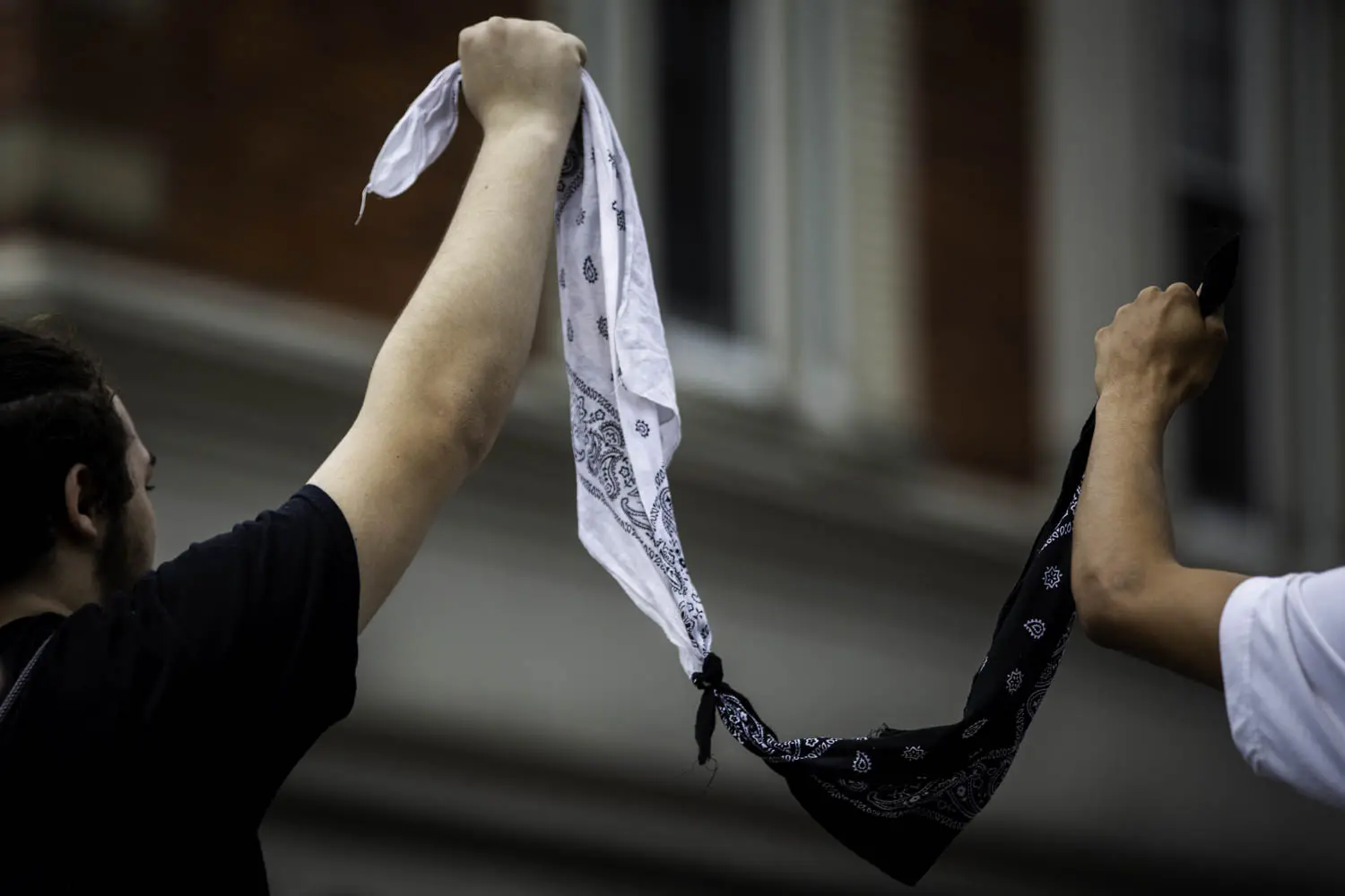 Two people hold white and black bandanas, tied together, between them.