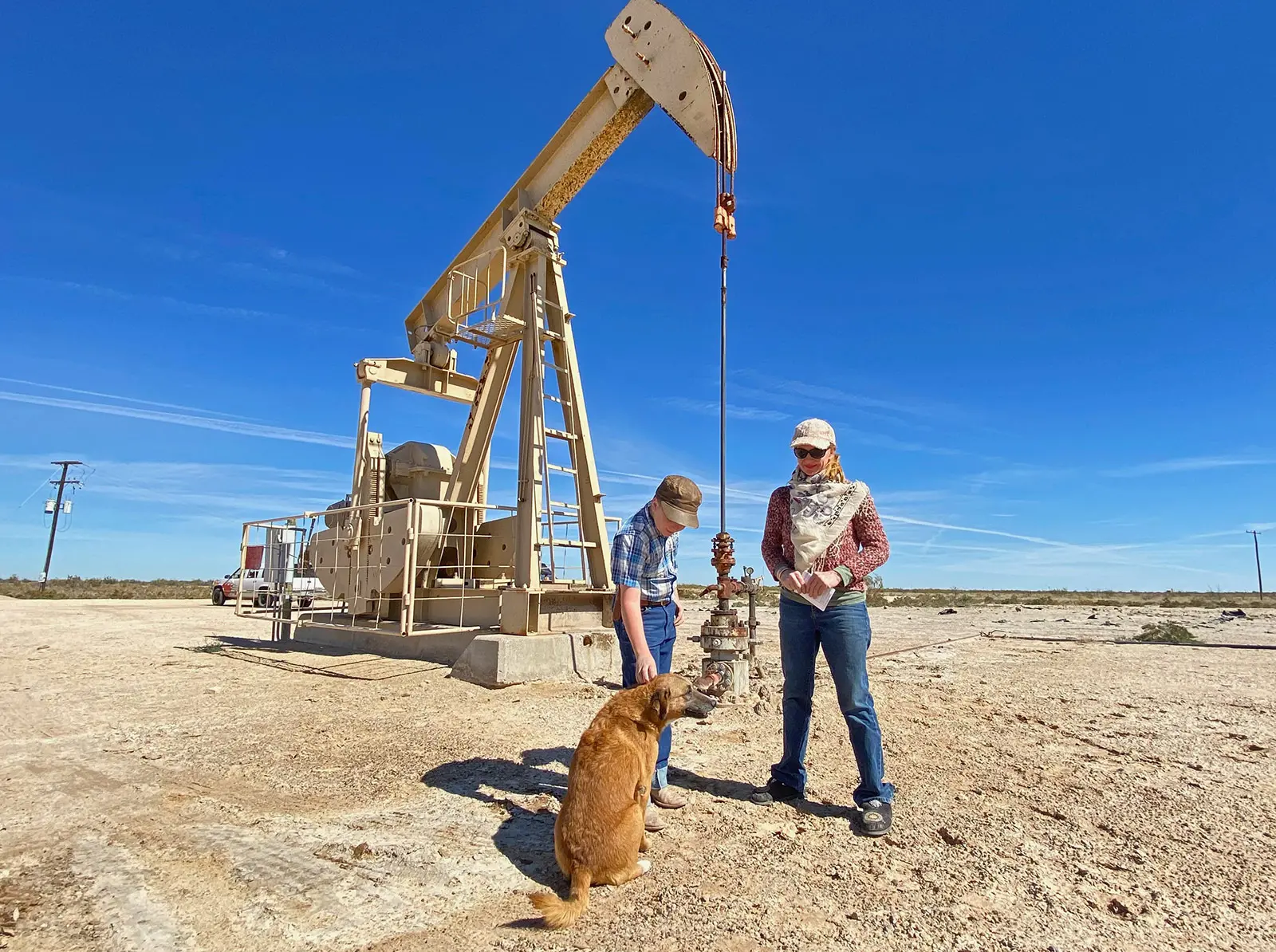 Two people and a dog stand in front of a well with extraction machinery.