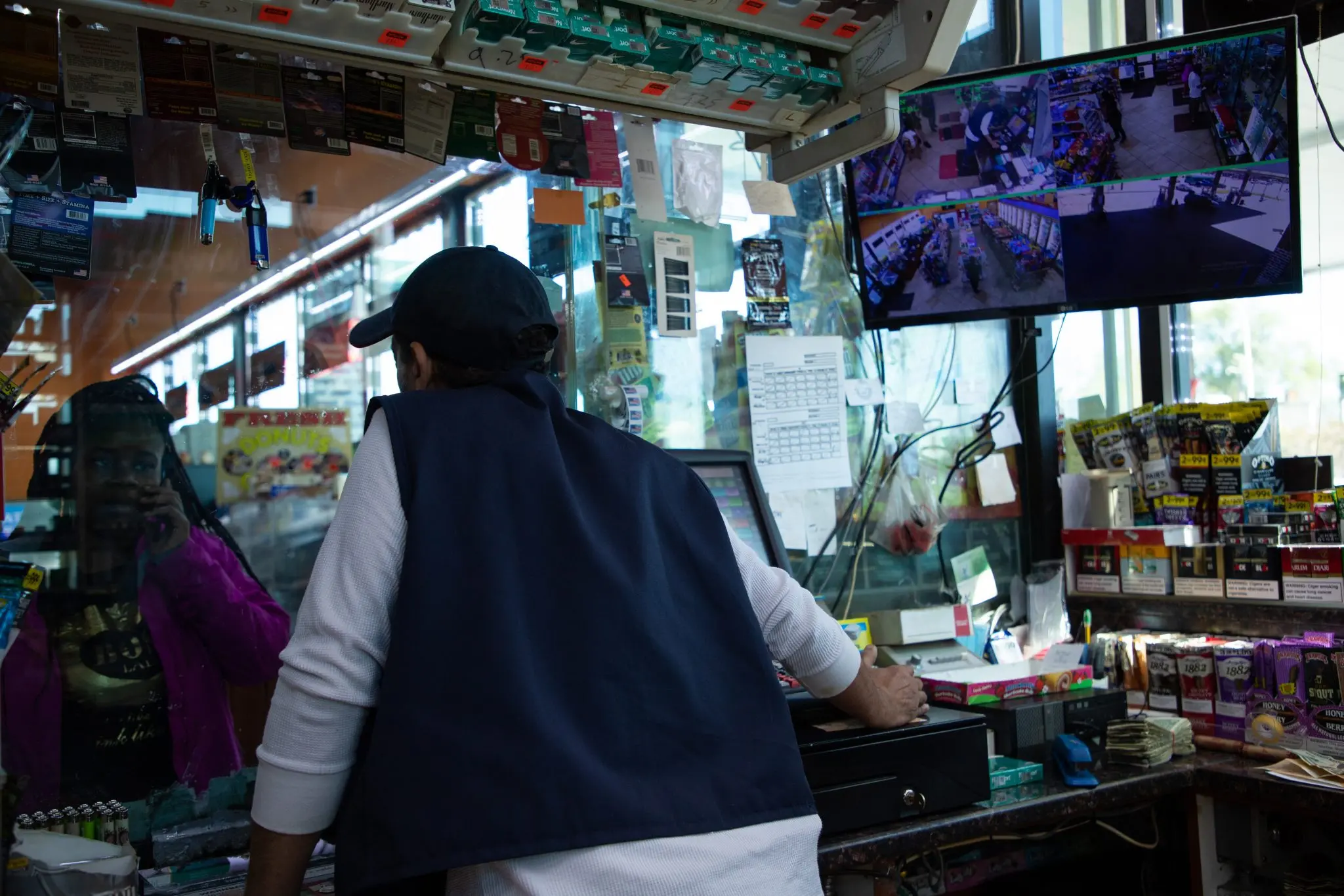 Ismail Salah serves a customer at the gas station he manages, with a security footage display in his view.