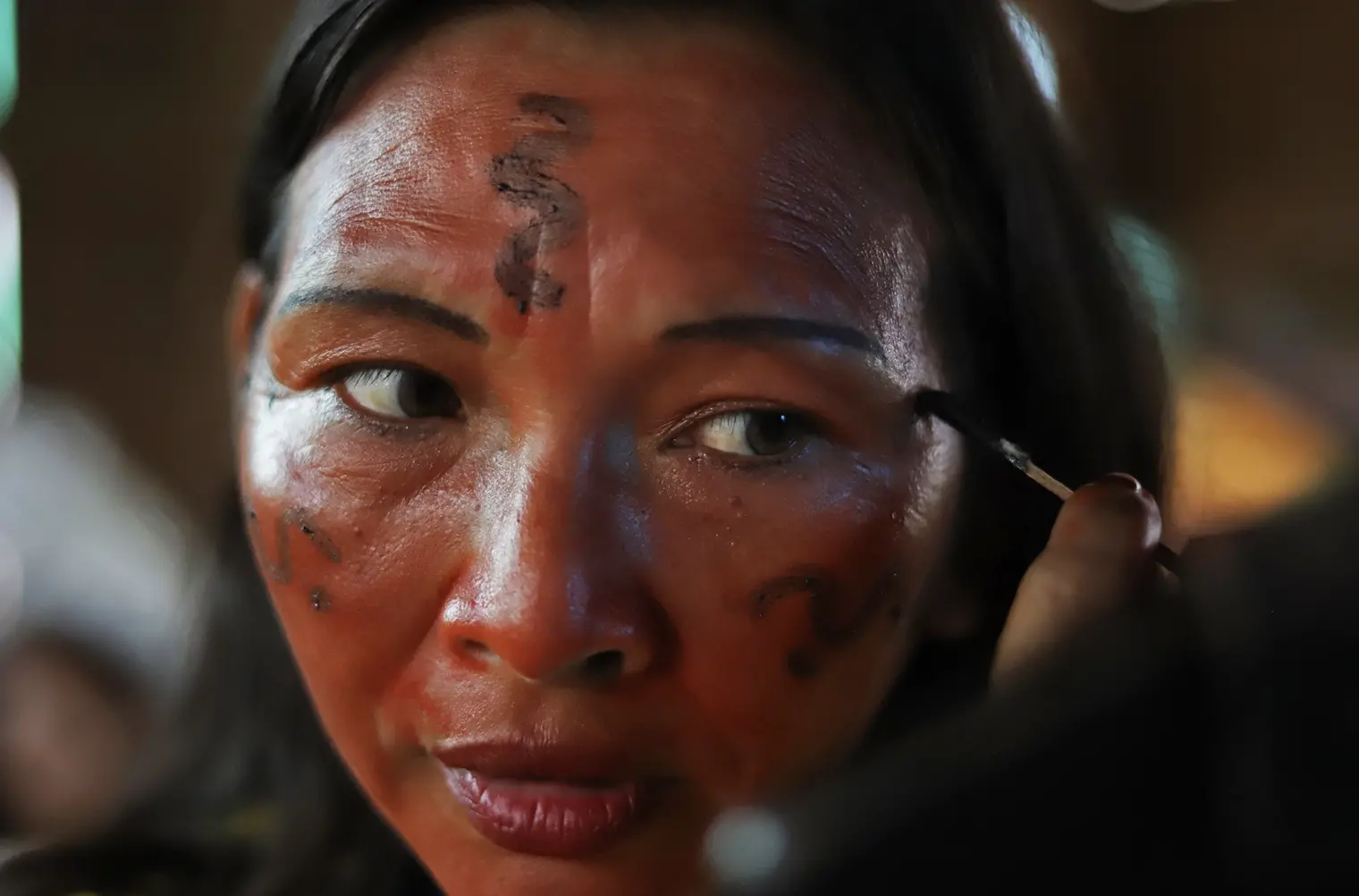 Photo of woman applying red paint to her face as part of an Indigenous tradition