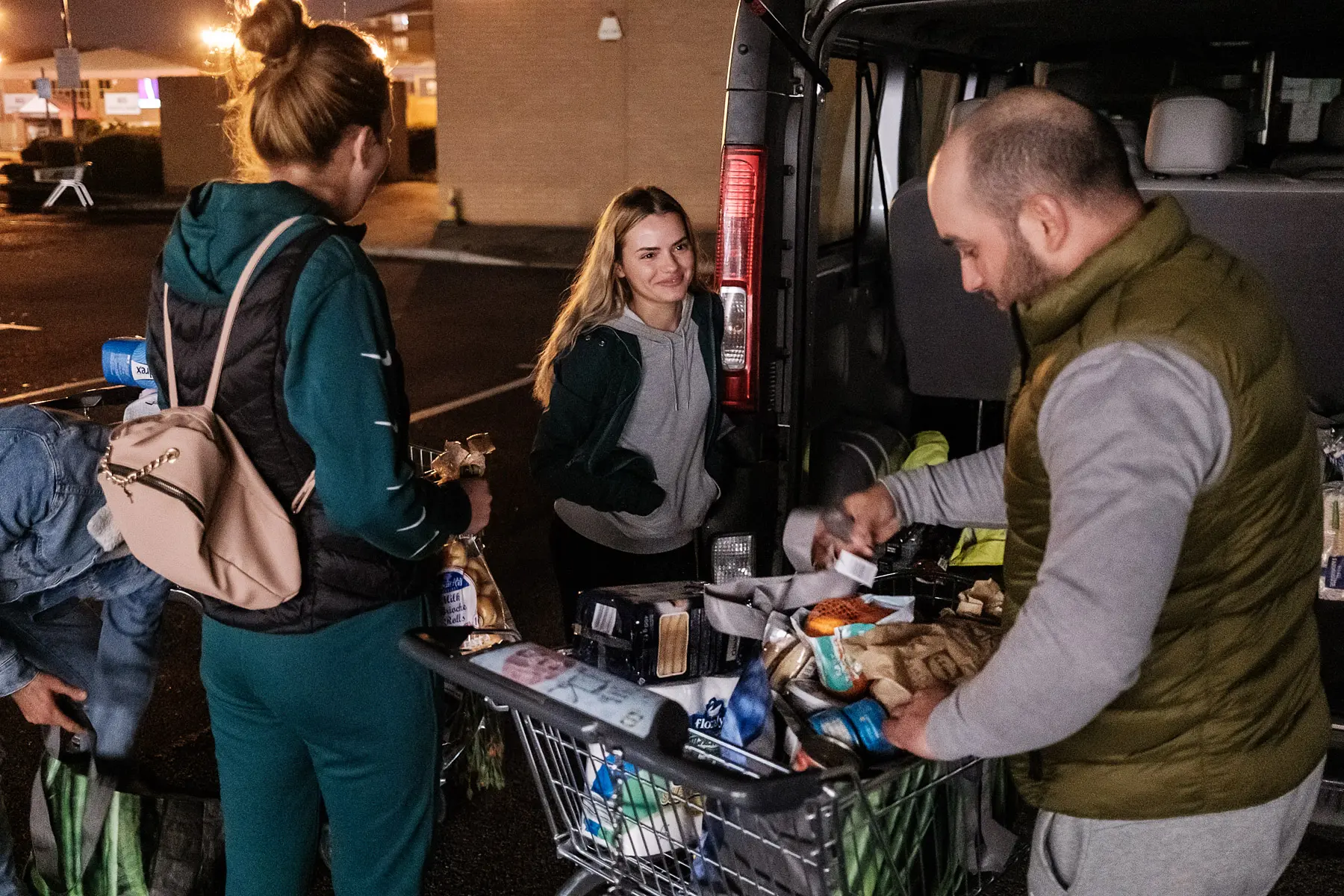 Young woman loads her groceries into a van with the help of a couple