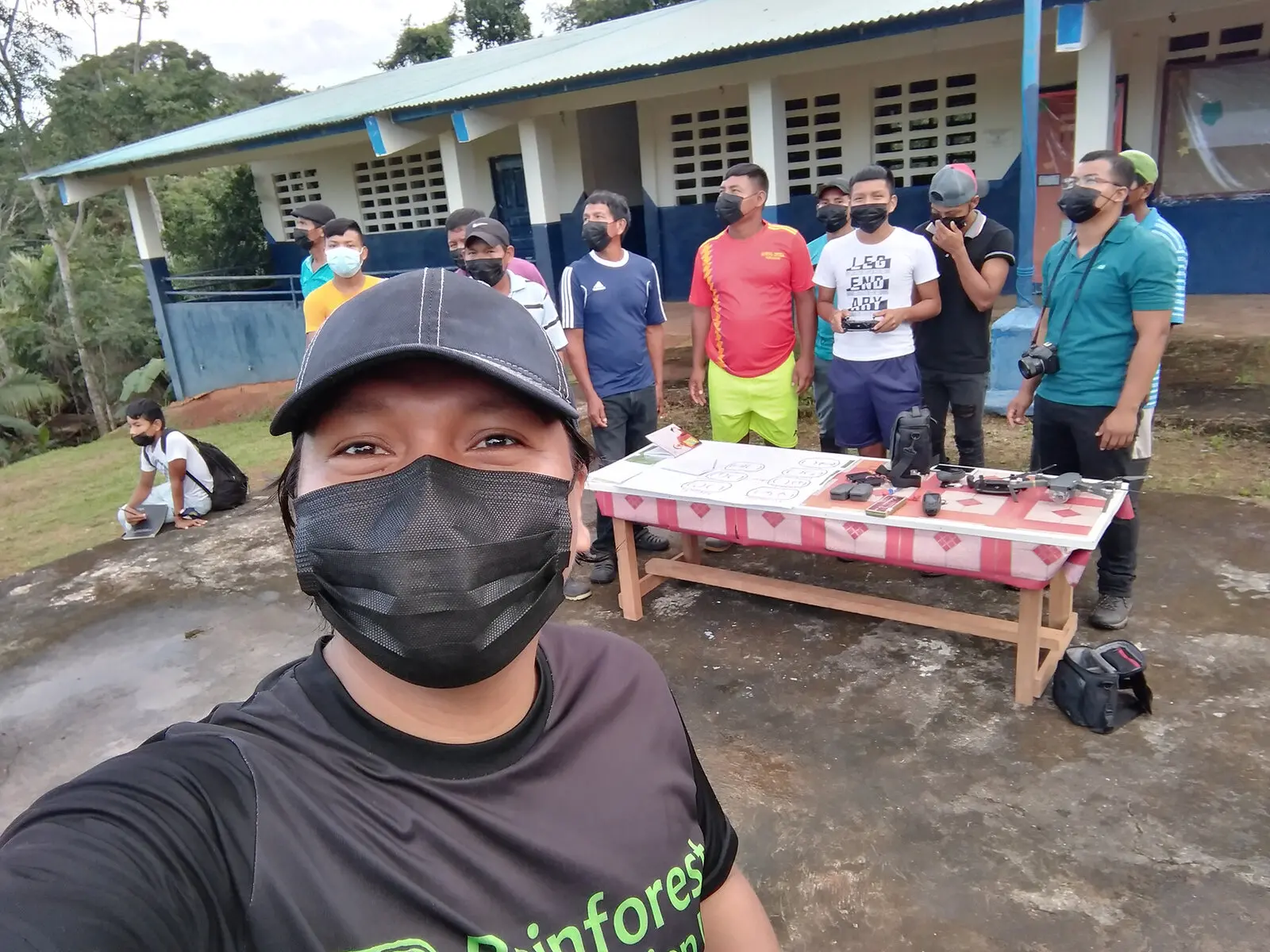 A person takes a selfie with a group of people standing in the background.