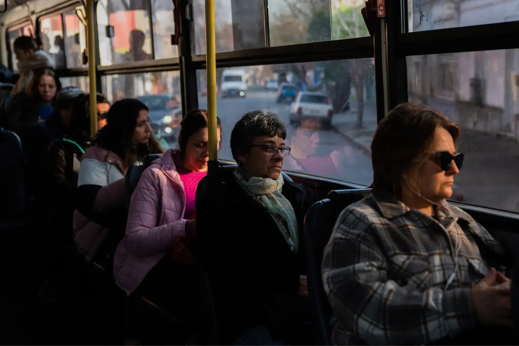People sit on a public bus. Seven people are in view sitting next to the window.
