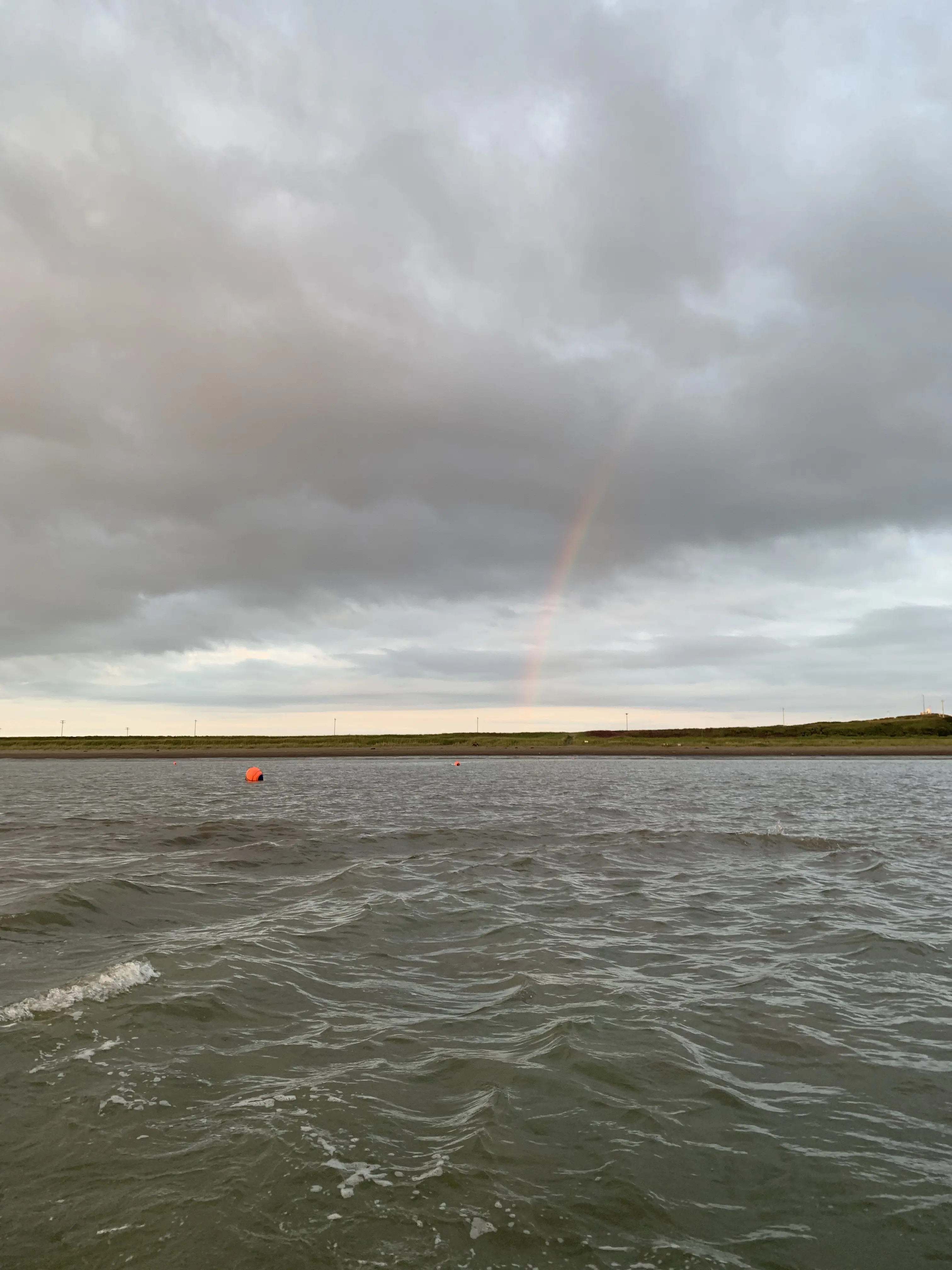 A rainbow peeks through the clouds over the water in Bristol Bay, Alaska.