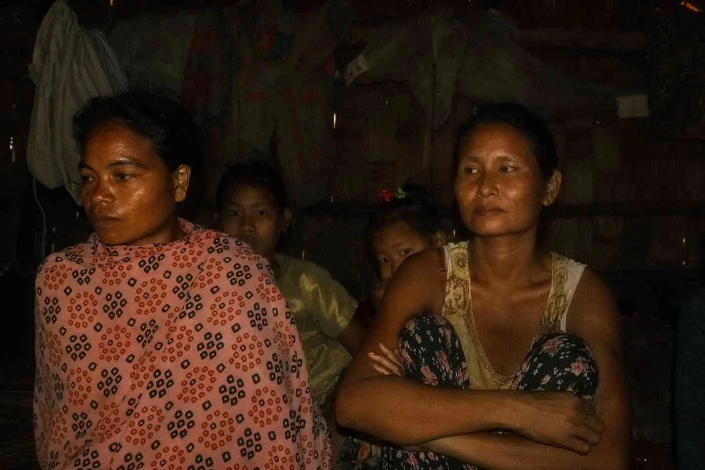 Two women in floral prints are lit by warm firelight at night.