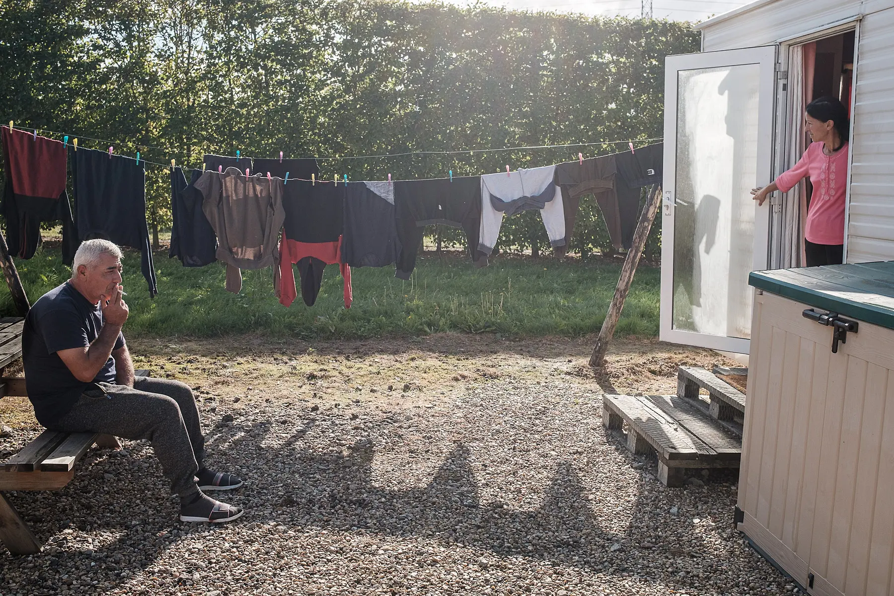 A man enjoys day off. He smokes a cigarette while clothes hang to dry outside the caravan