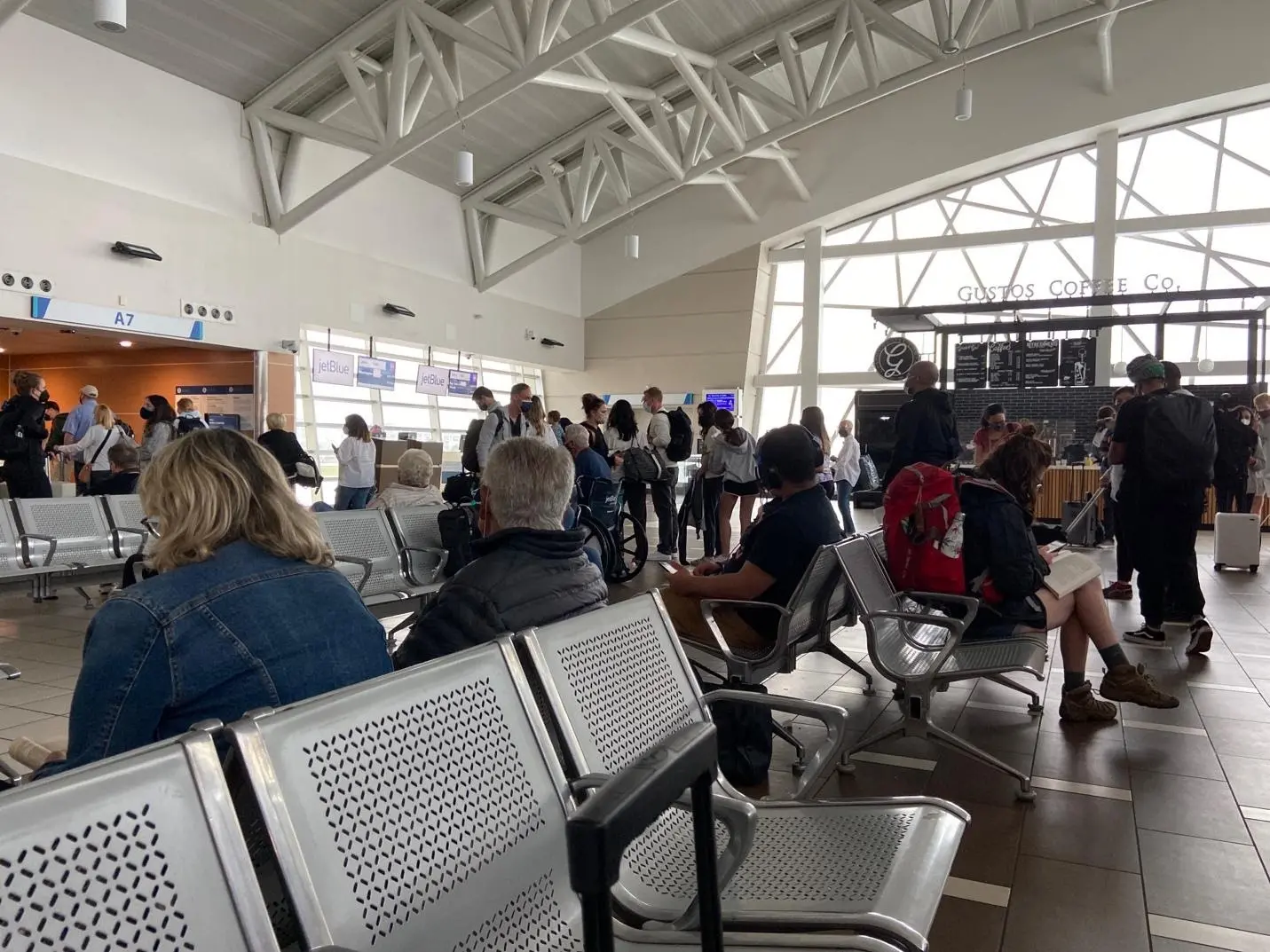 View of airplane terminal with passengers standing and waiting in chairs.