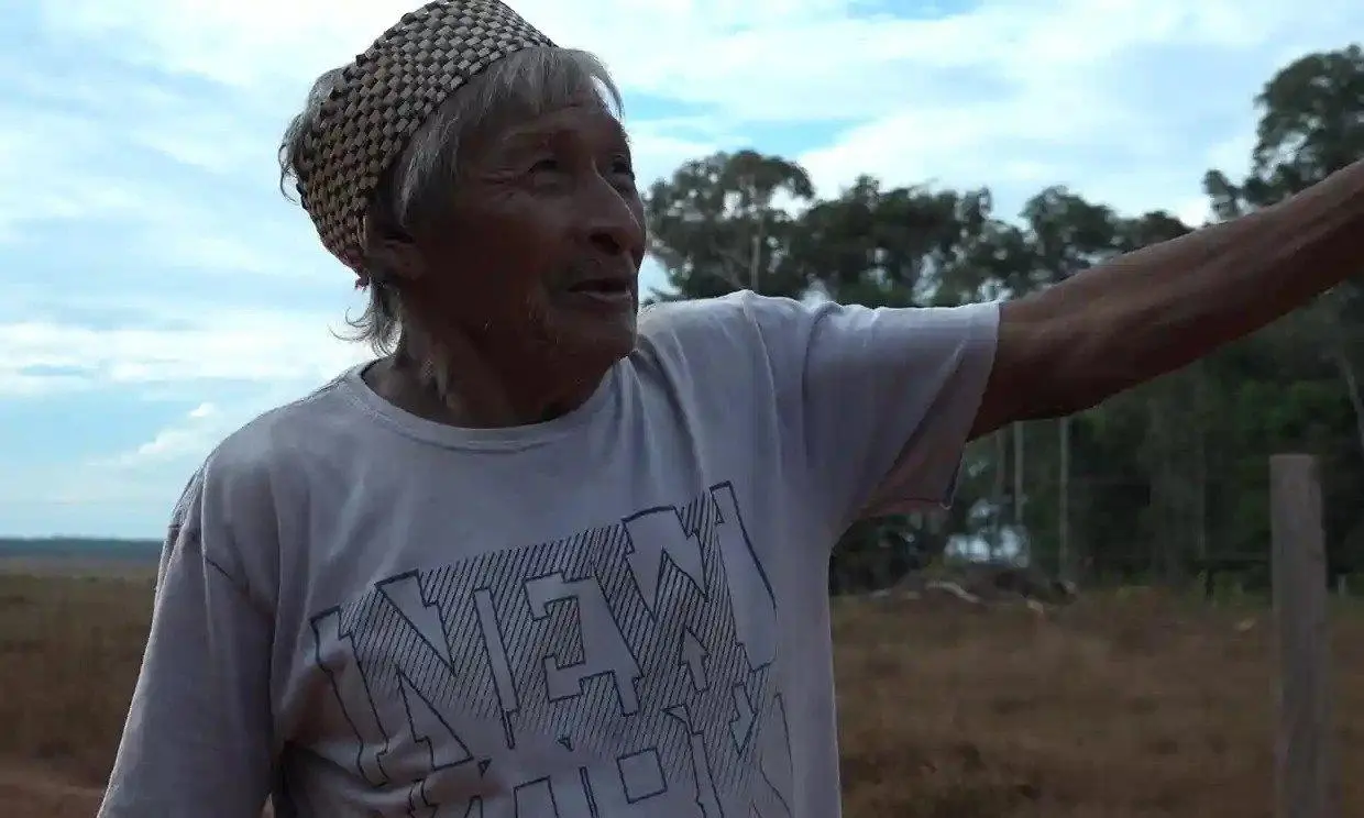 A man gestures while speaking, wearing a traditional headband and a New York t-shirt.