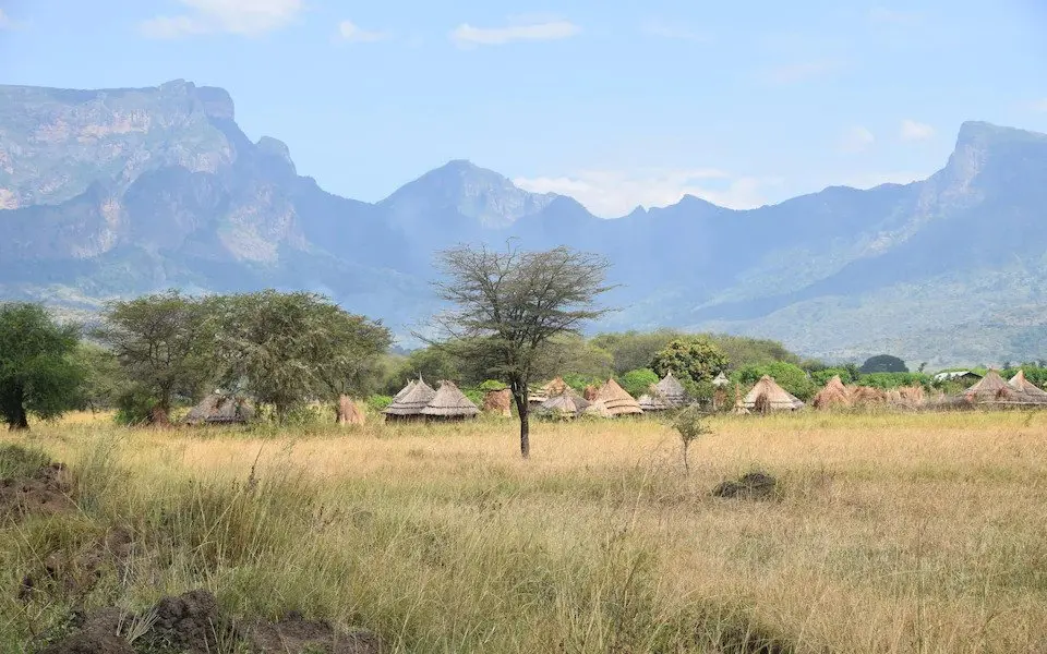 a thatched roof village with verdant mountains in the background