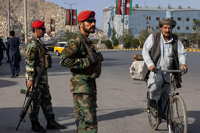 Soldiers stand in front of neighborhood while man bikes by