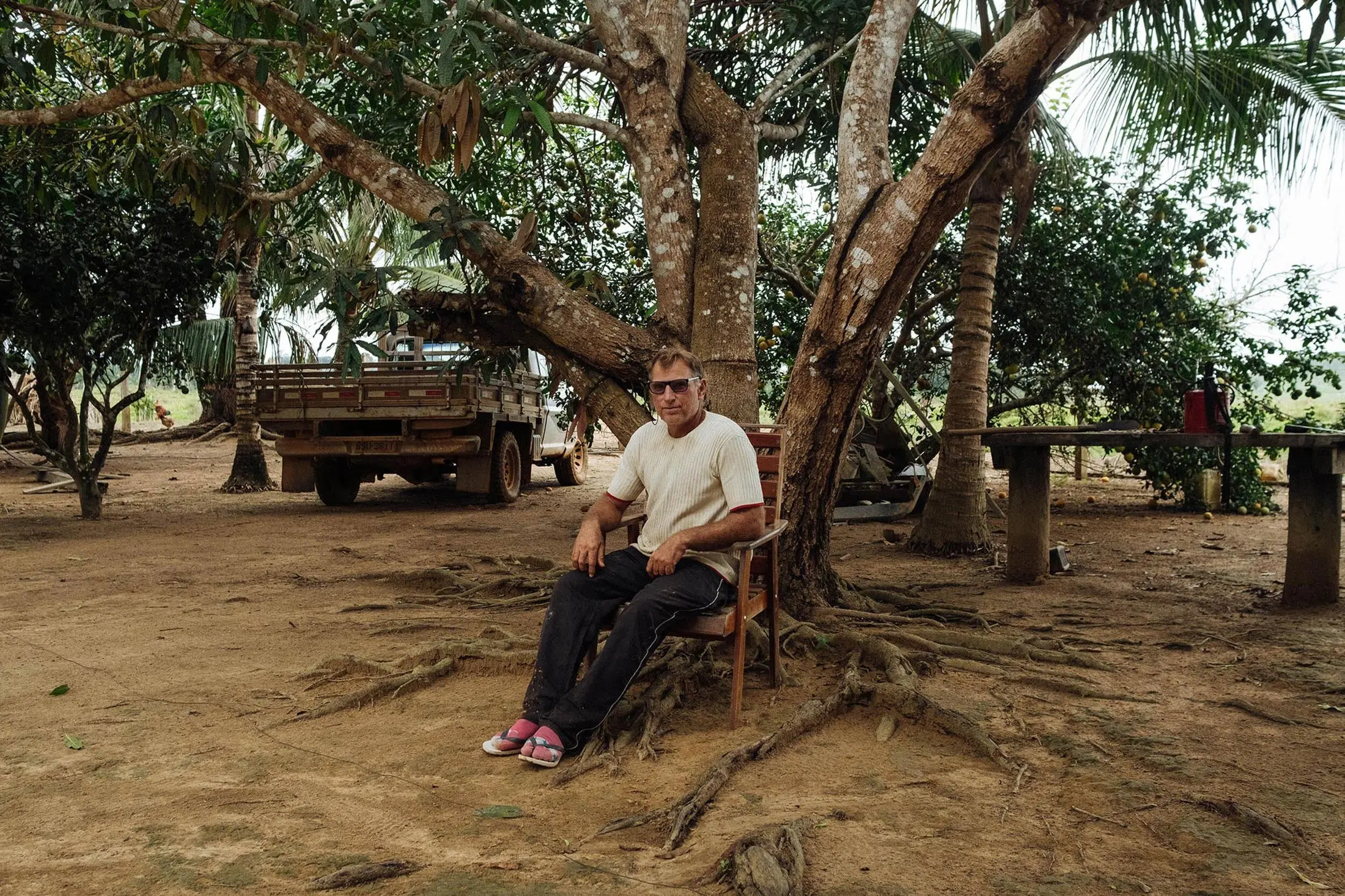 Man sits in a wood chair on former rainforest land that he now owns