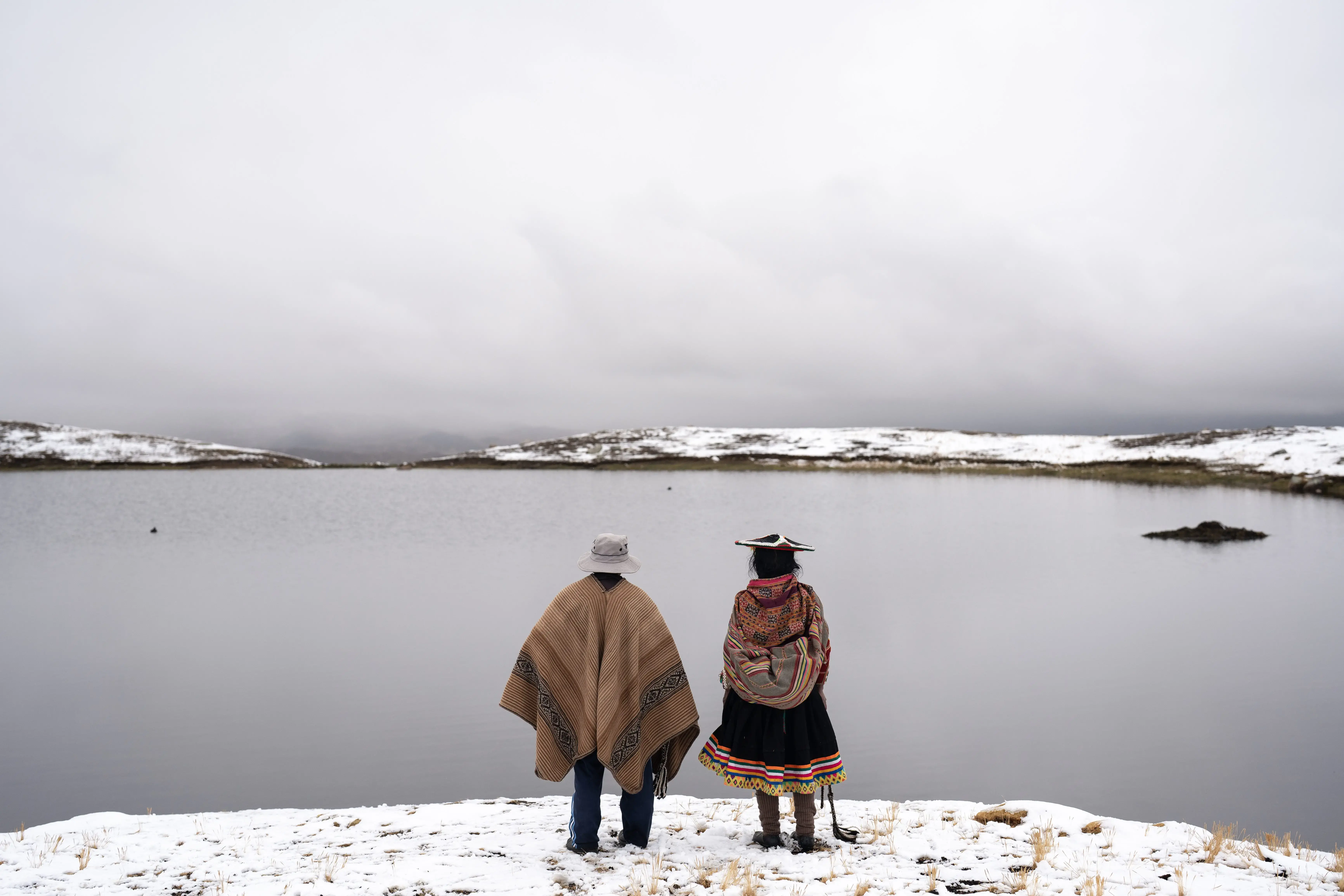 Two people look out over the lake at the foot of the snow-capped Quelccaya.