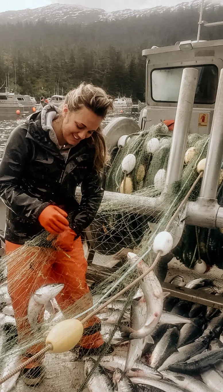 Kinsey Justa holds a net with fish on a boat.