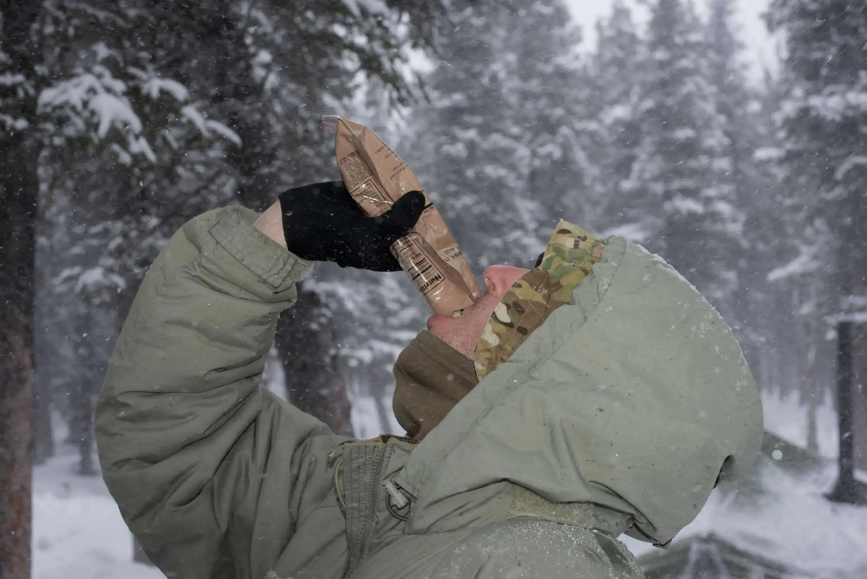 Close-up of a soldier with his head tilted back, pouring a packet of food directly into his mouth.