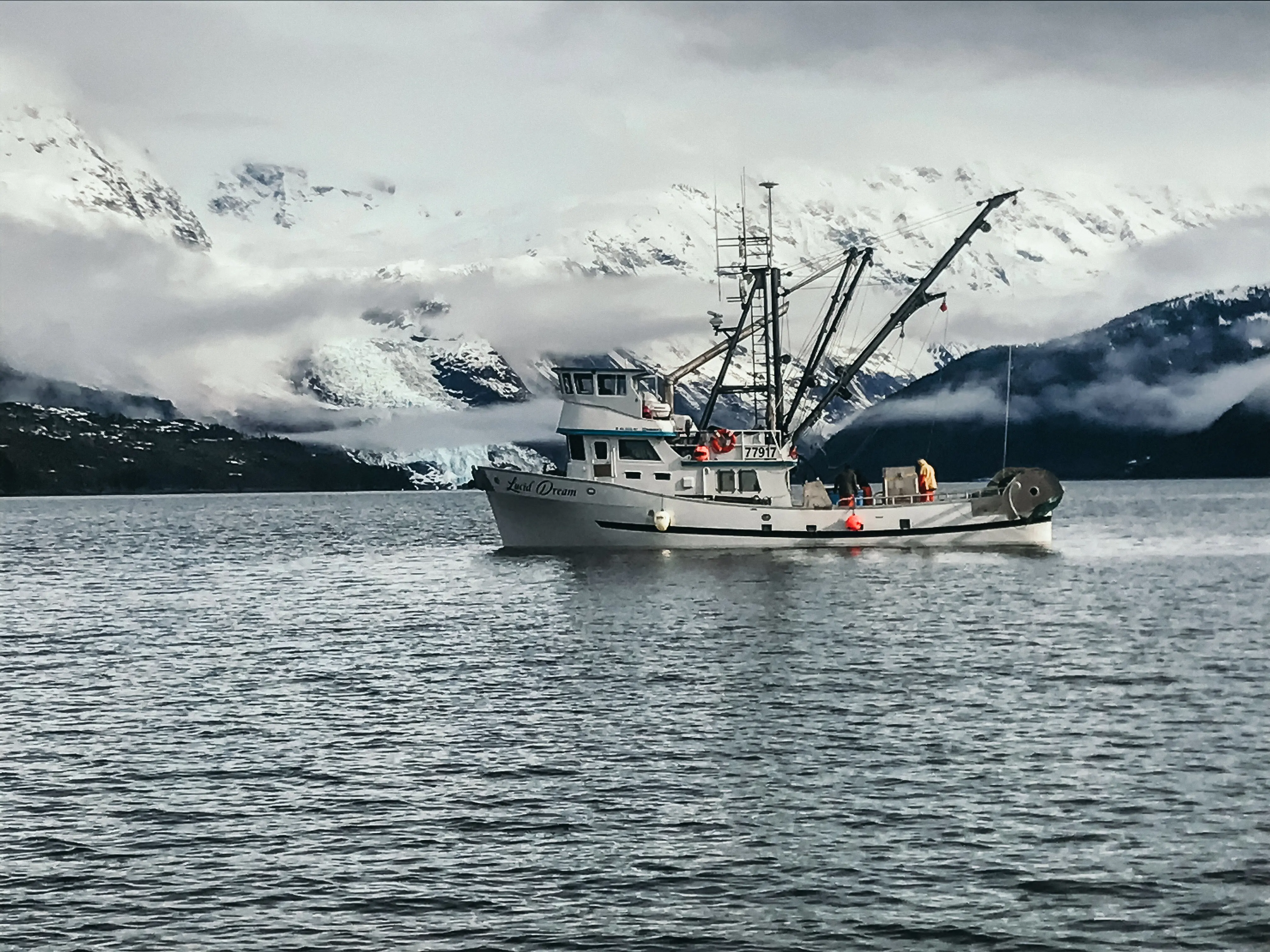 A boat sits in the water. There are snow-covered mountains in the background.