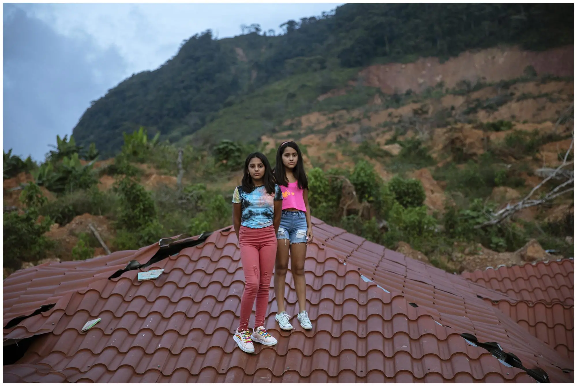 Two twins stand on a roof of their neighbor's house