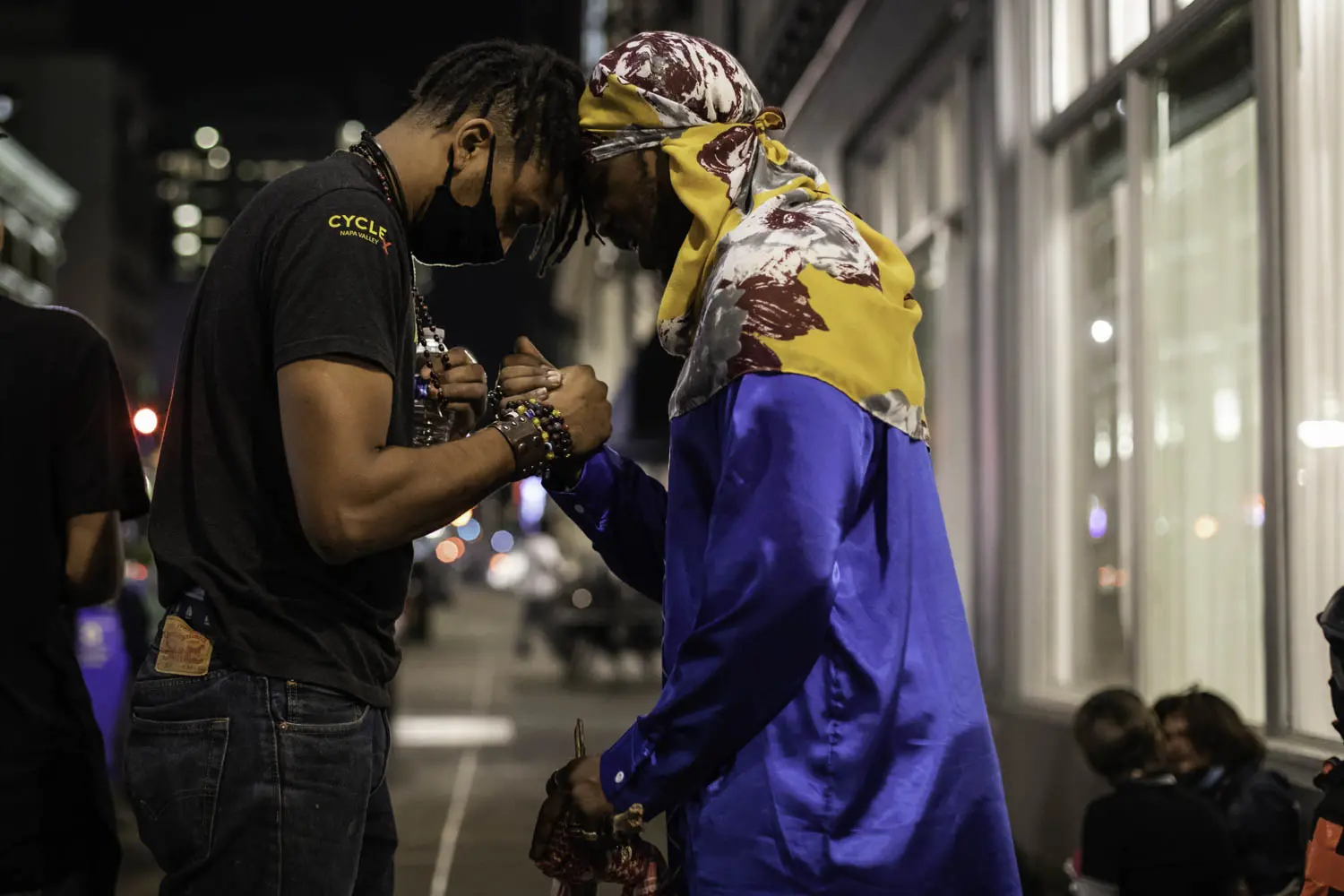 Two men bow their heads together in prayer and grasp hands.