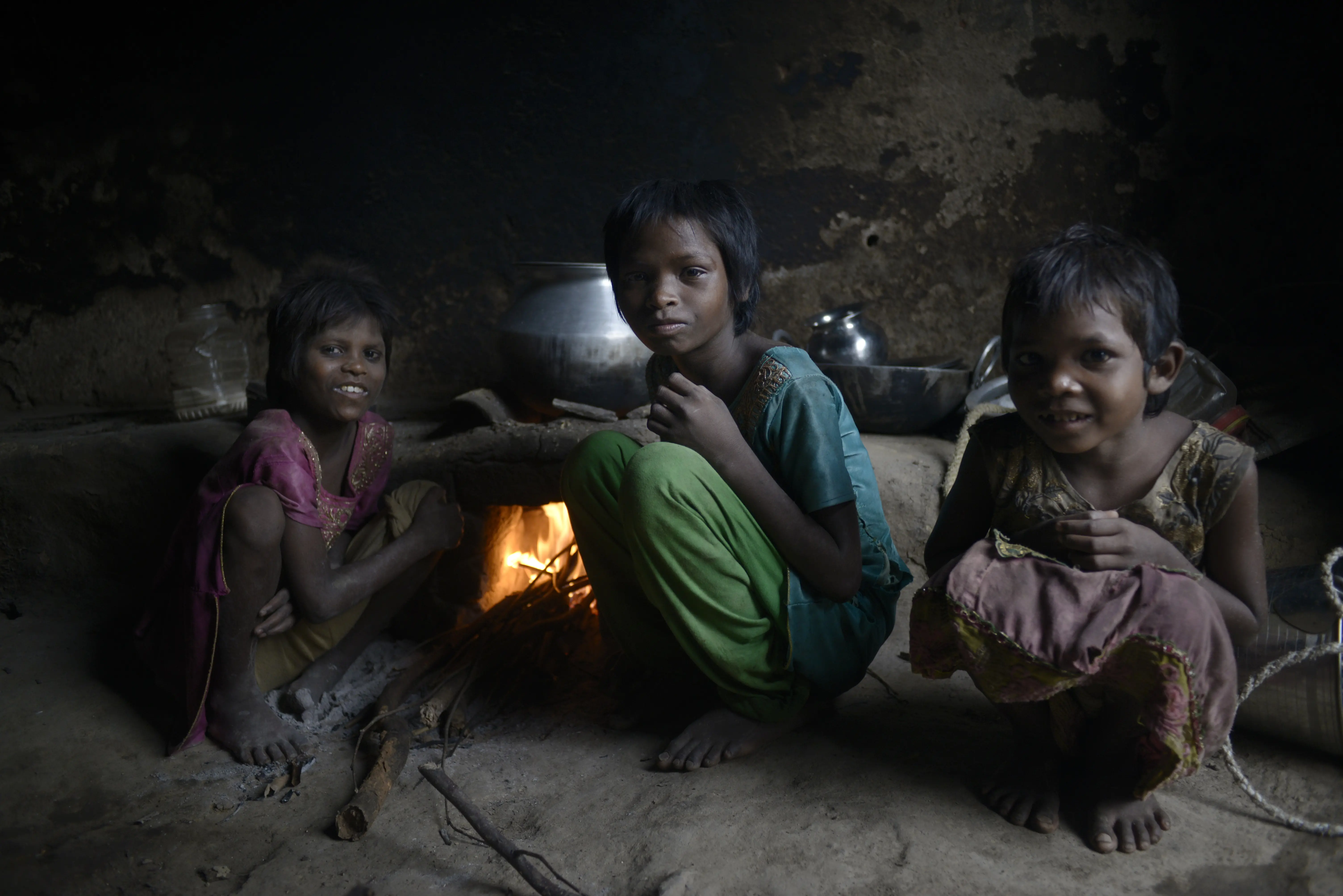 Three young children sit together around a fire