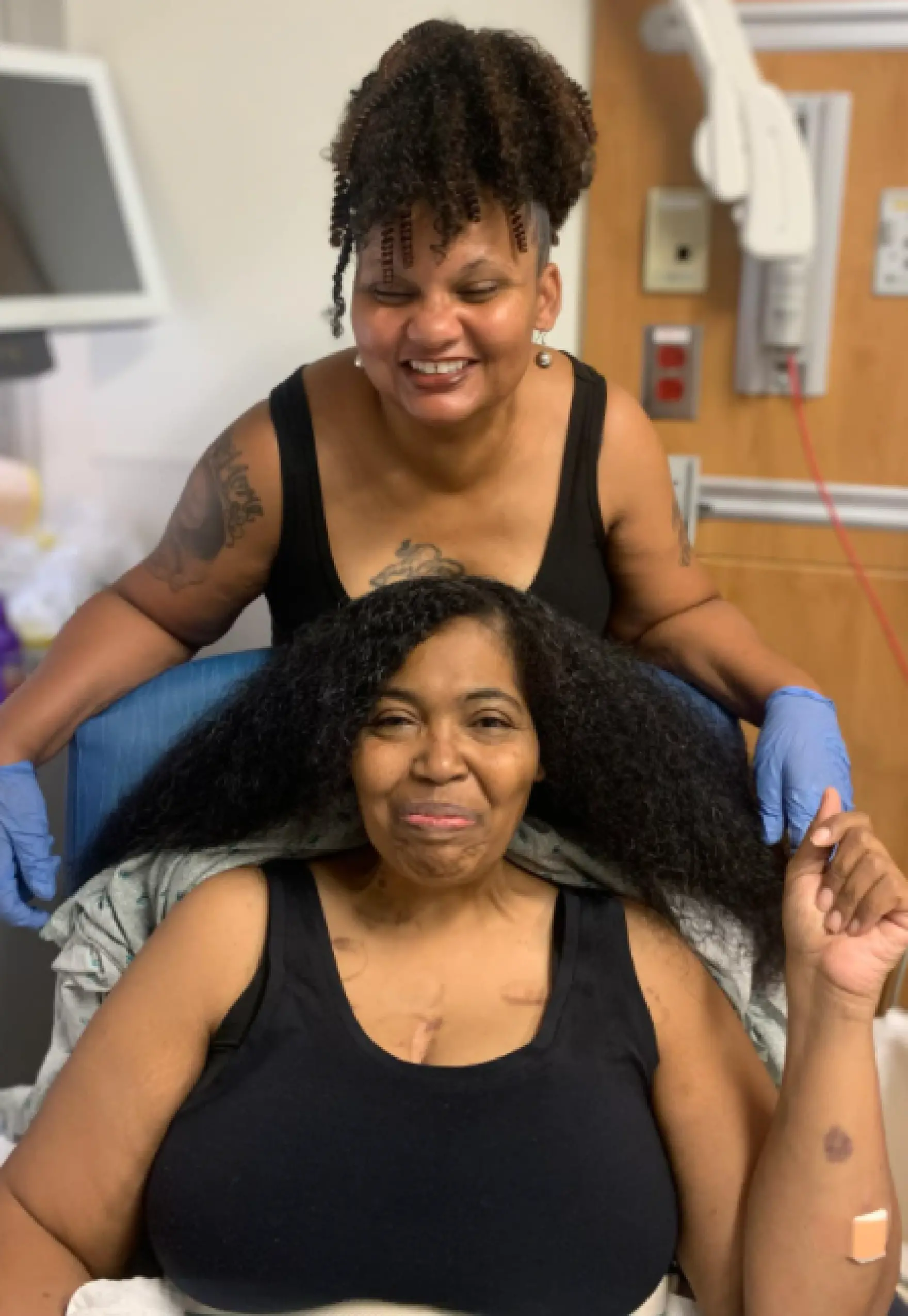 Kim Daniels and her sister smile in a photo. Hospital room wires and gear are seen in the background.