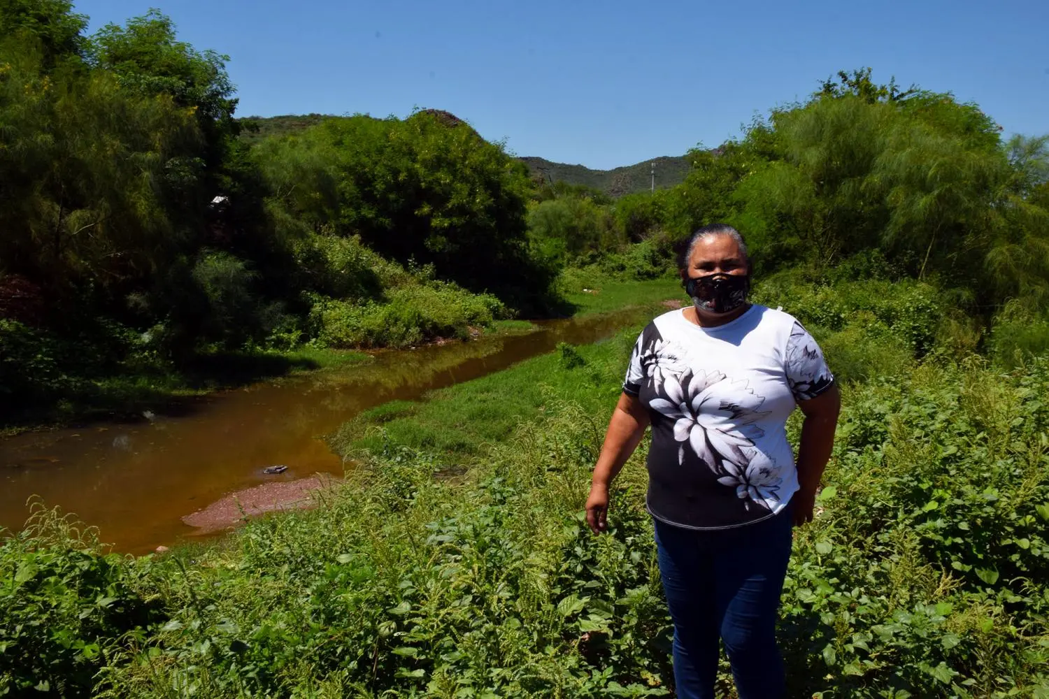 A woman stands near a pond of water sewage near her house