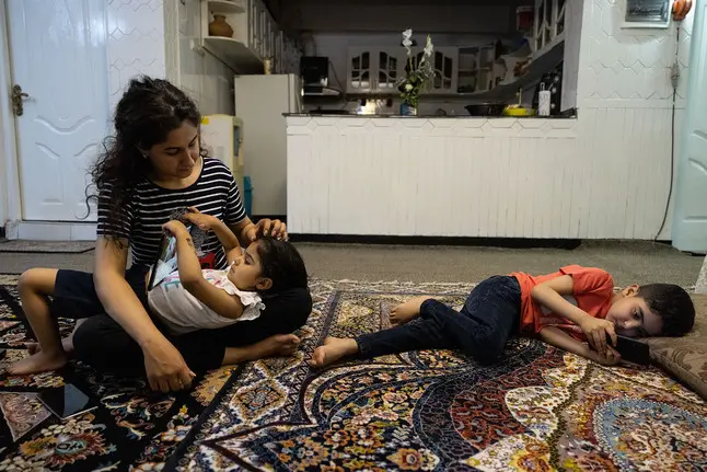 A young woman sits with her children in their apartment