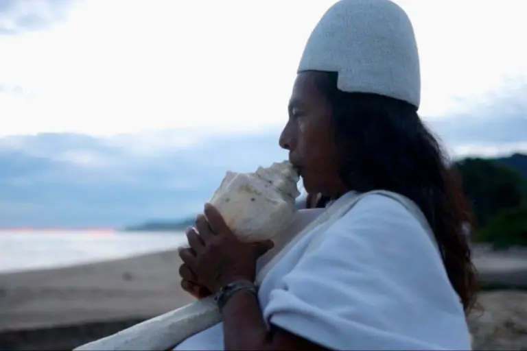 Indigenous person blows into a shell