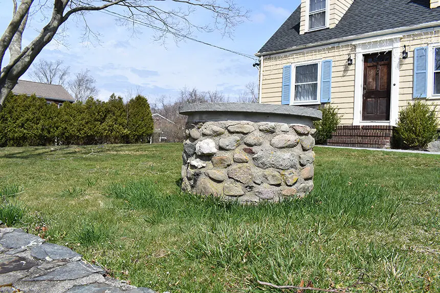 Image shows a stone well in the front yard of a yellow house in Rhode Island.