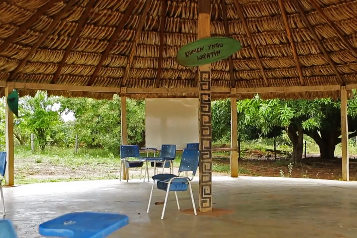 Photo of an Indigenous school with a small blue desks, a white board, and a green sign.