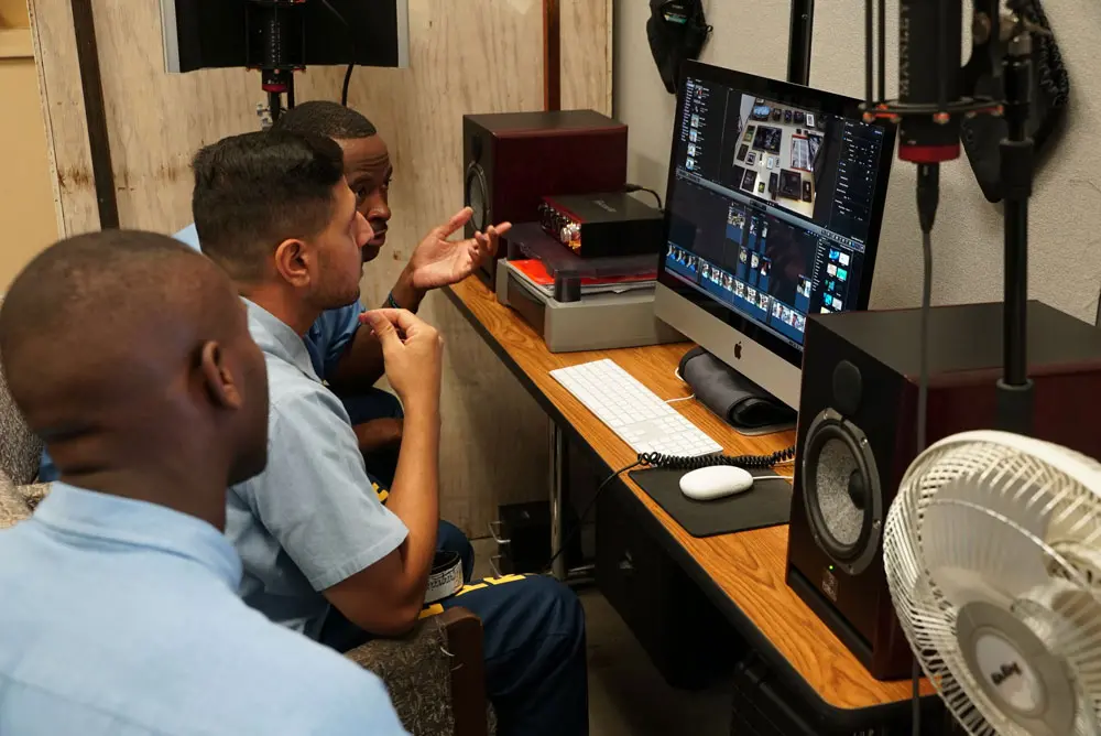 Three people sit, discussing, in front of a computer.