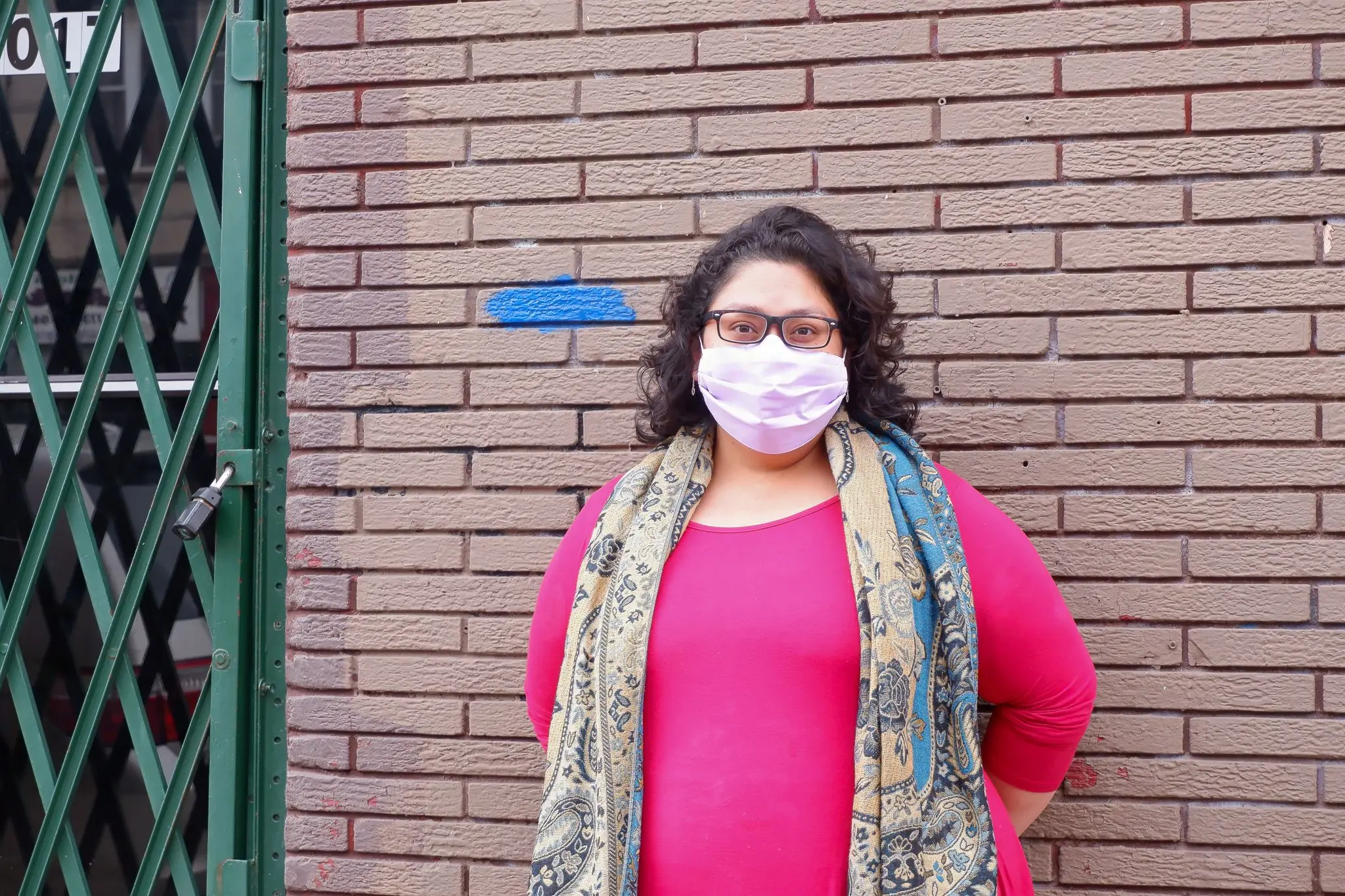 woman stands masked in front of brick building