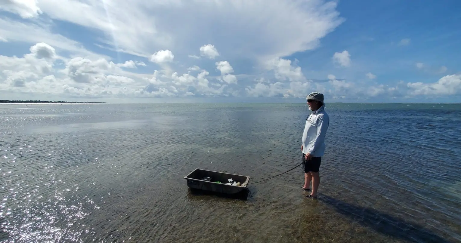 Man stands in ocean and looks out with a small fishing boat of supplies