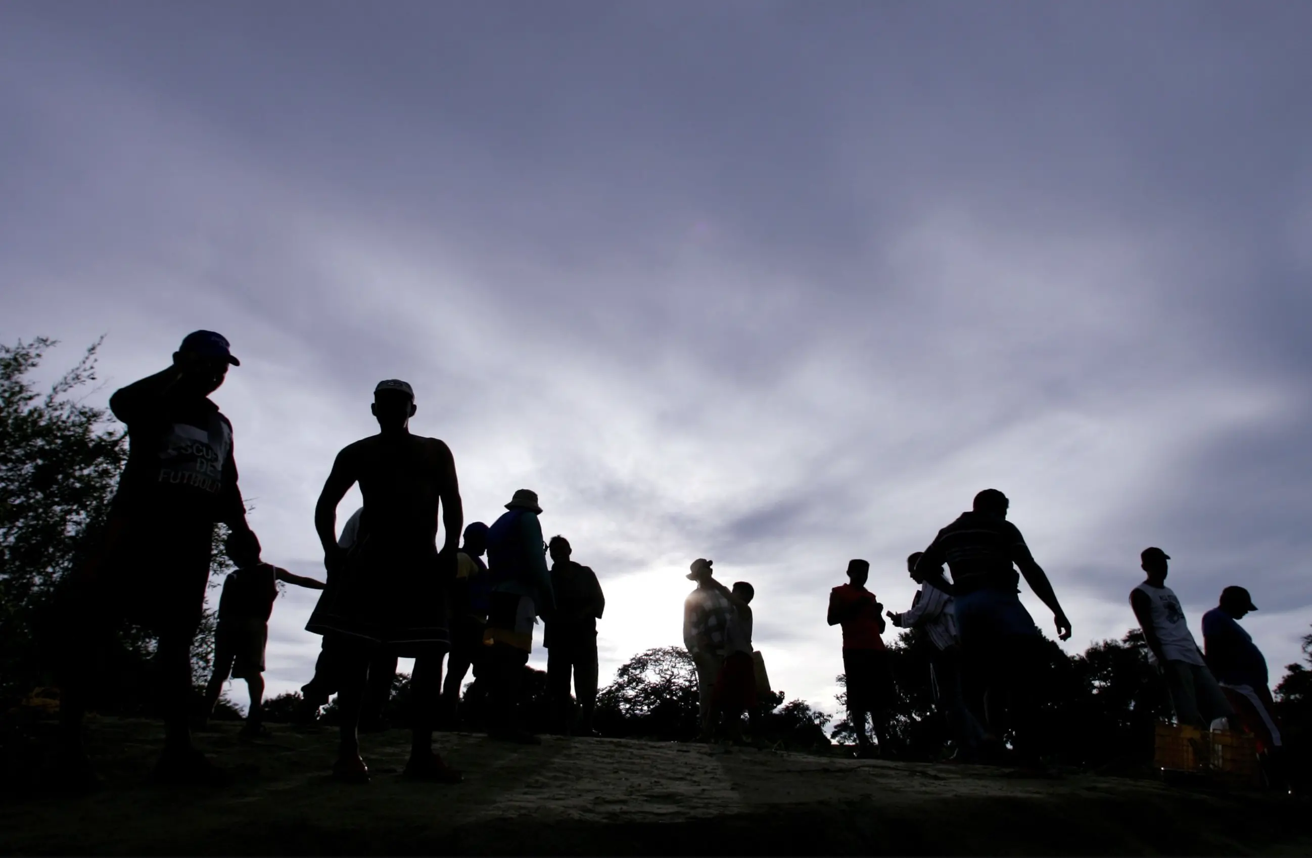 The fish sellers are grouped together. Only the sky is in focus, while the silhouettes of the men are in the foreground. 