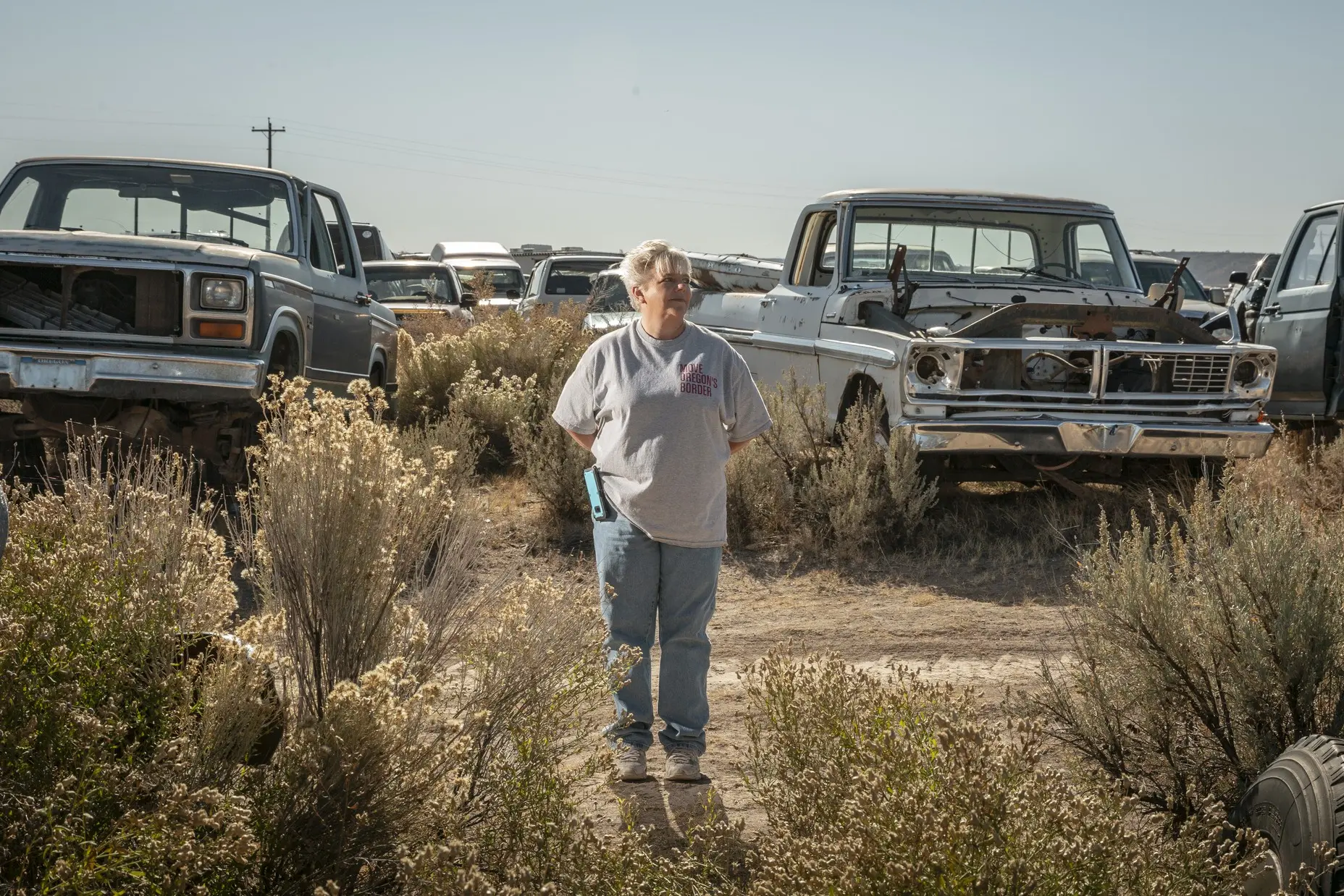 Woman stands in front of cars in an abandonded car lot