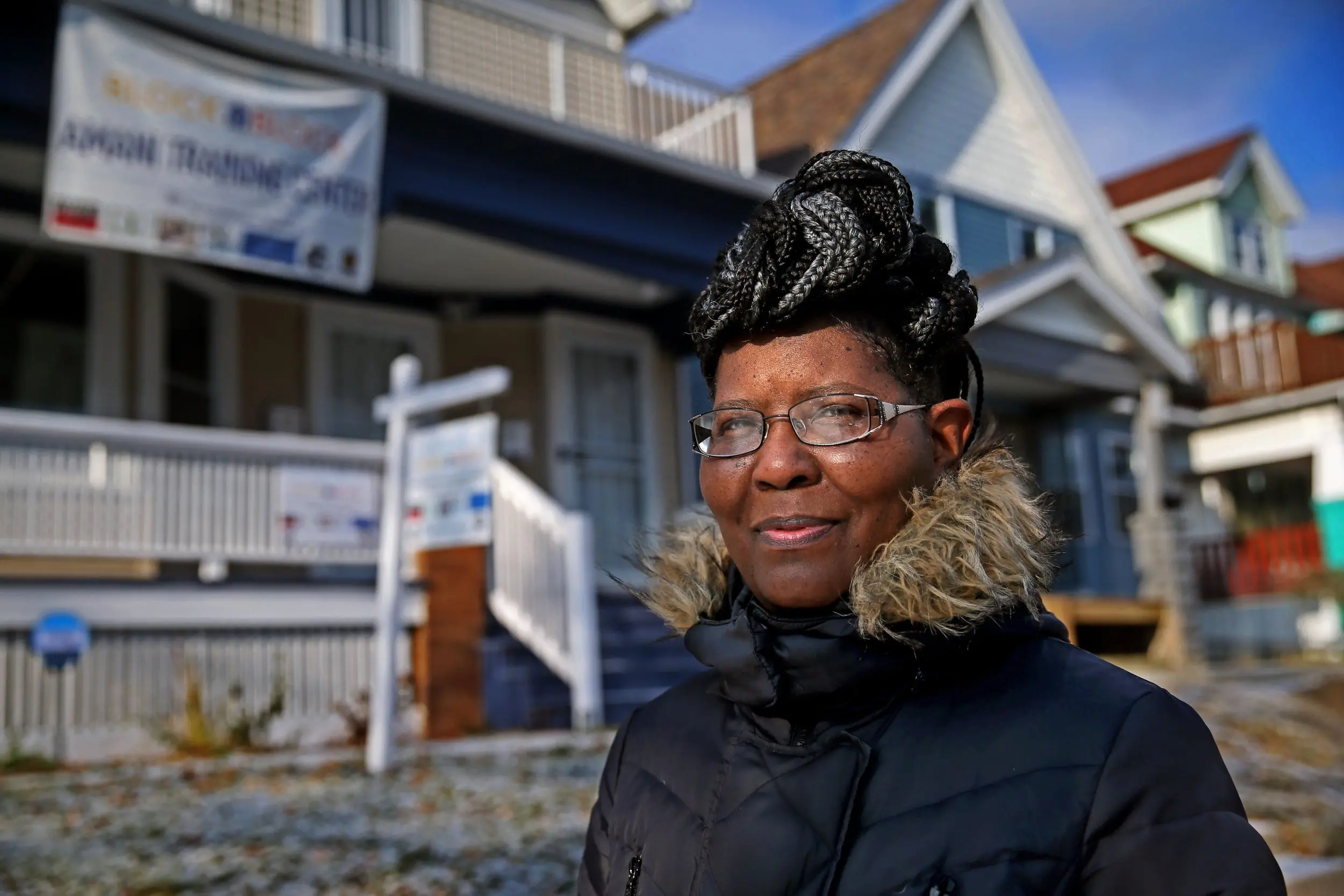 Woman stands in parka in front of a home for sale