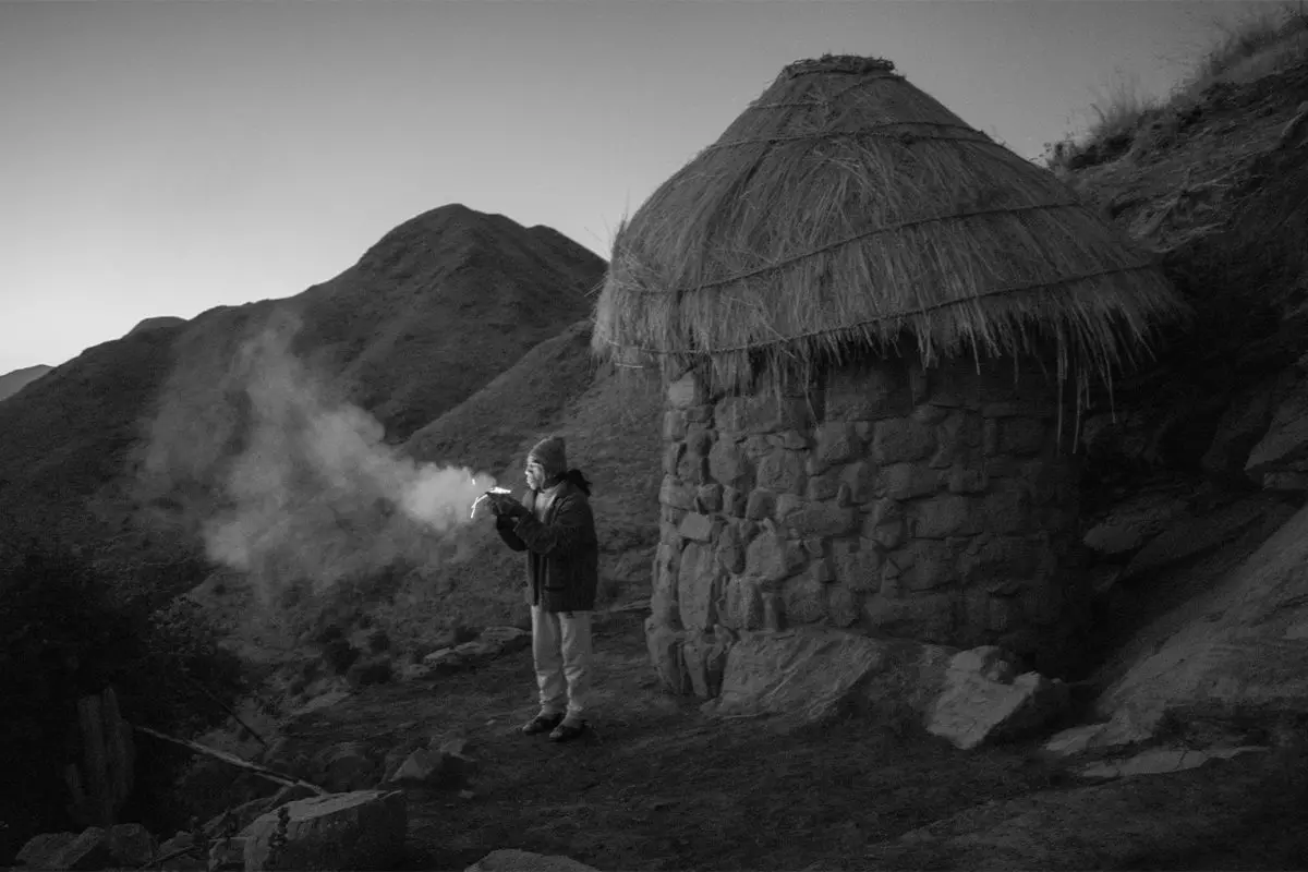 Man burns palo santo outside brick hut