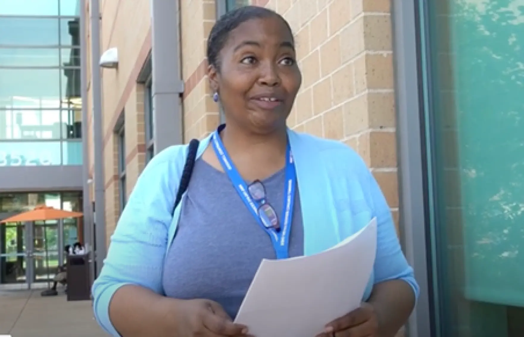 Woman wearing a lanyard stands holding papers outside of a building