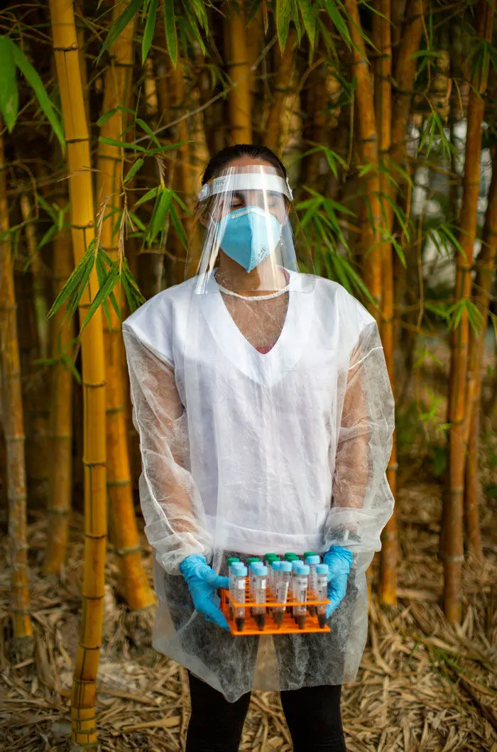 A person in PPE holds vials while standing outside.