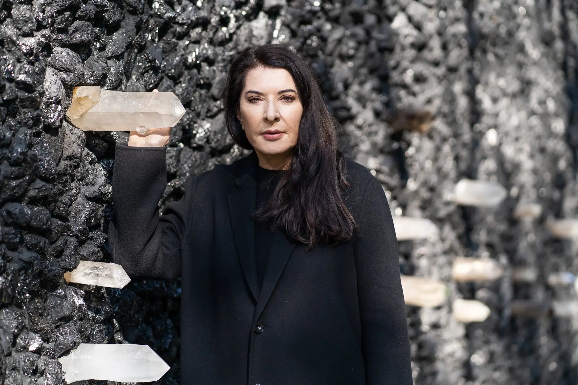 Woman stands in black coat holding a crystal attached to the memorial