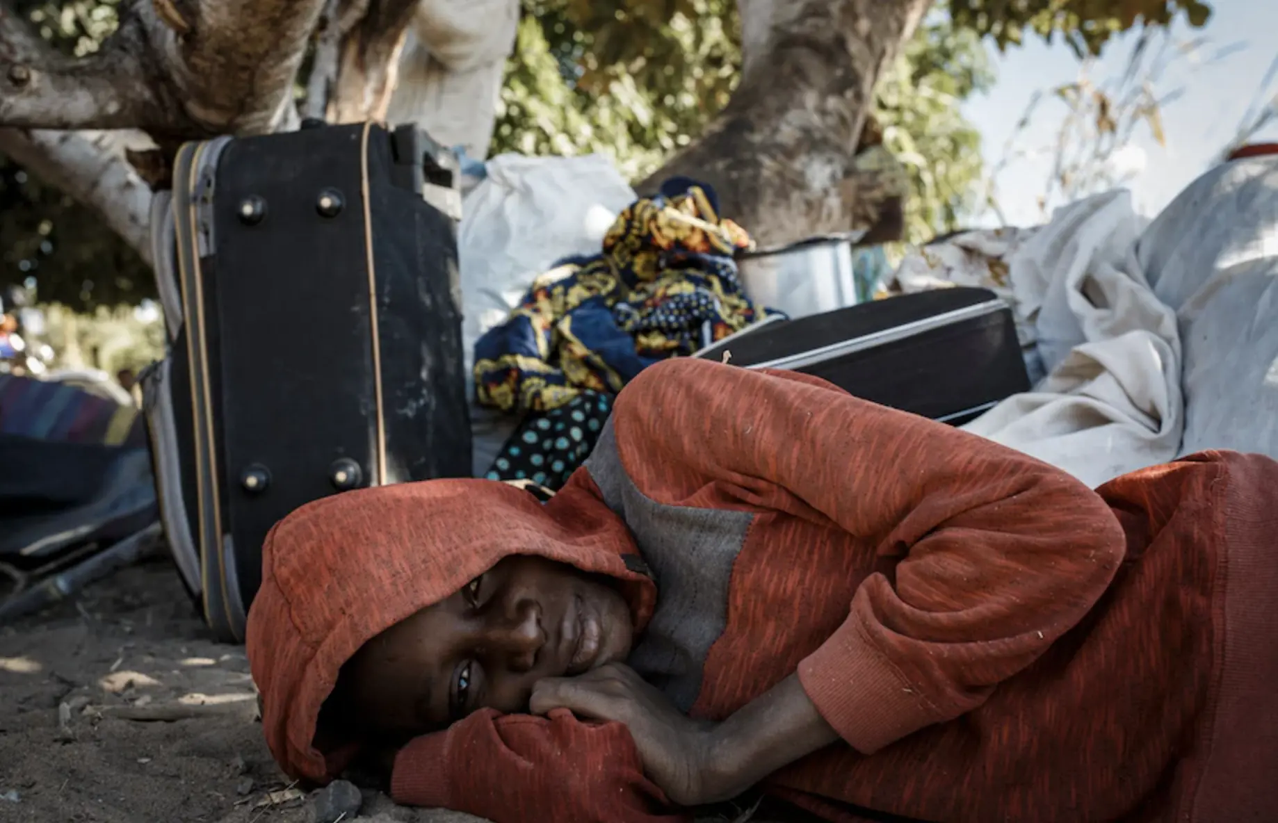 boy lays on ground in front pile of suitcases