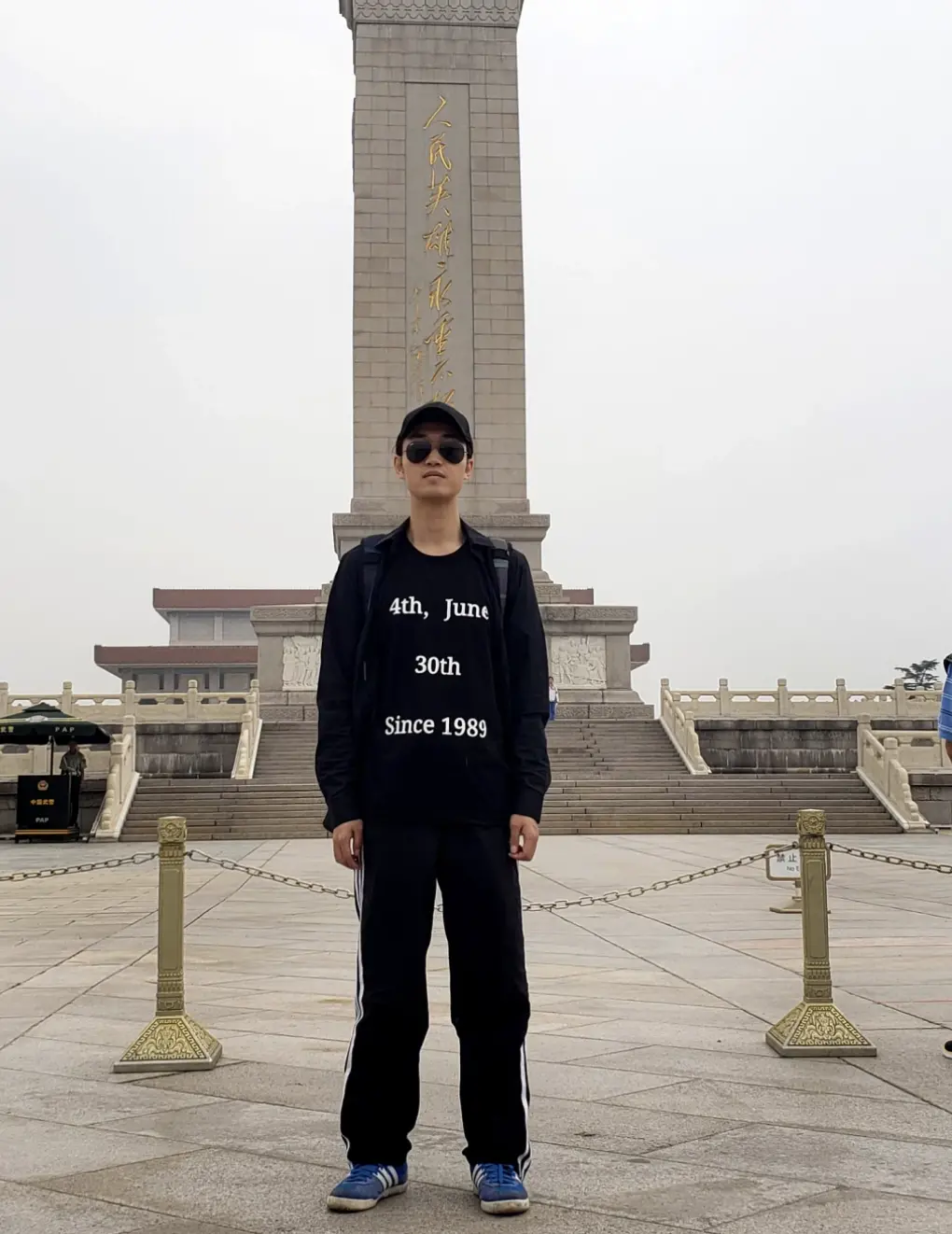 Dong Zehua stands in front of Tiananmen Square monument in Beijing in China in a black shirt that says " 4th June 30th Since 1989" in black sunglasses.