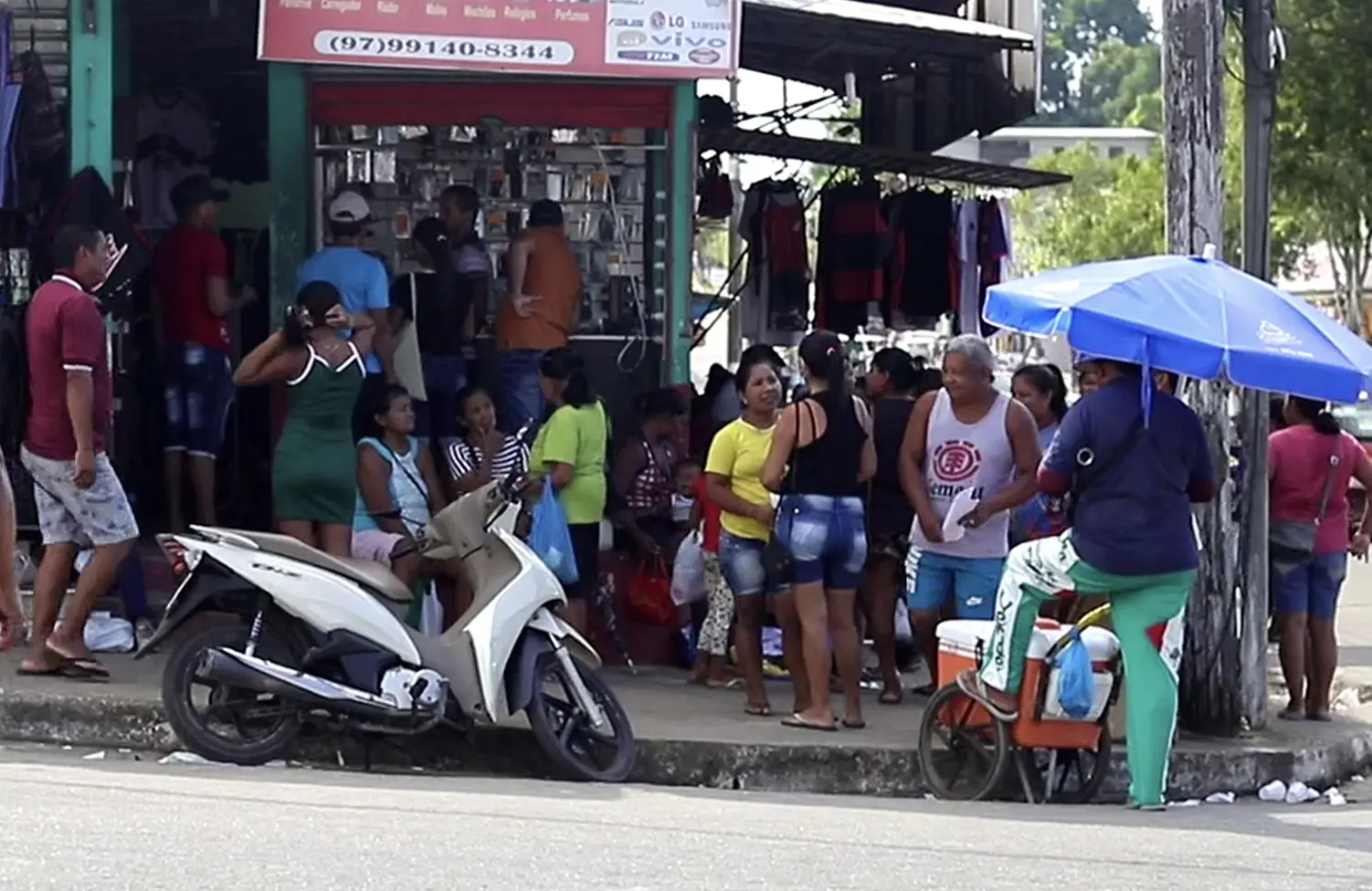 Photo of bustling shopping street  with vendors selling clothes and a motorcycle parked 