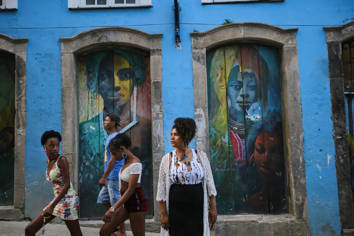 A portrait of Rutian Pataxó in front of a building with murals on it.