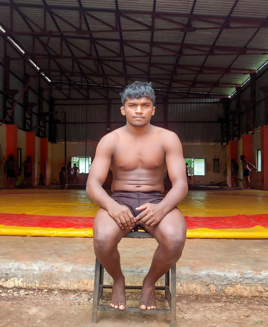 young guy sits on a stool in a wrestling space in rural India
