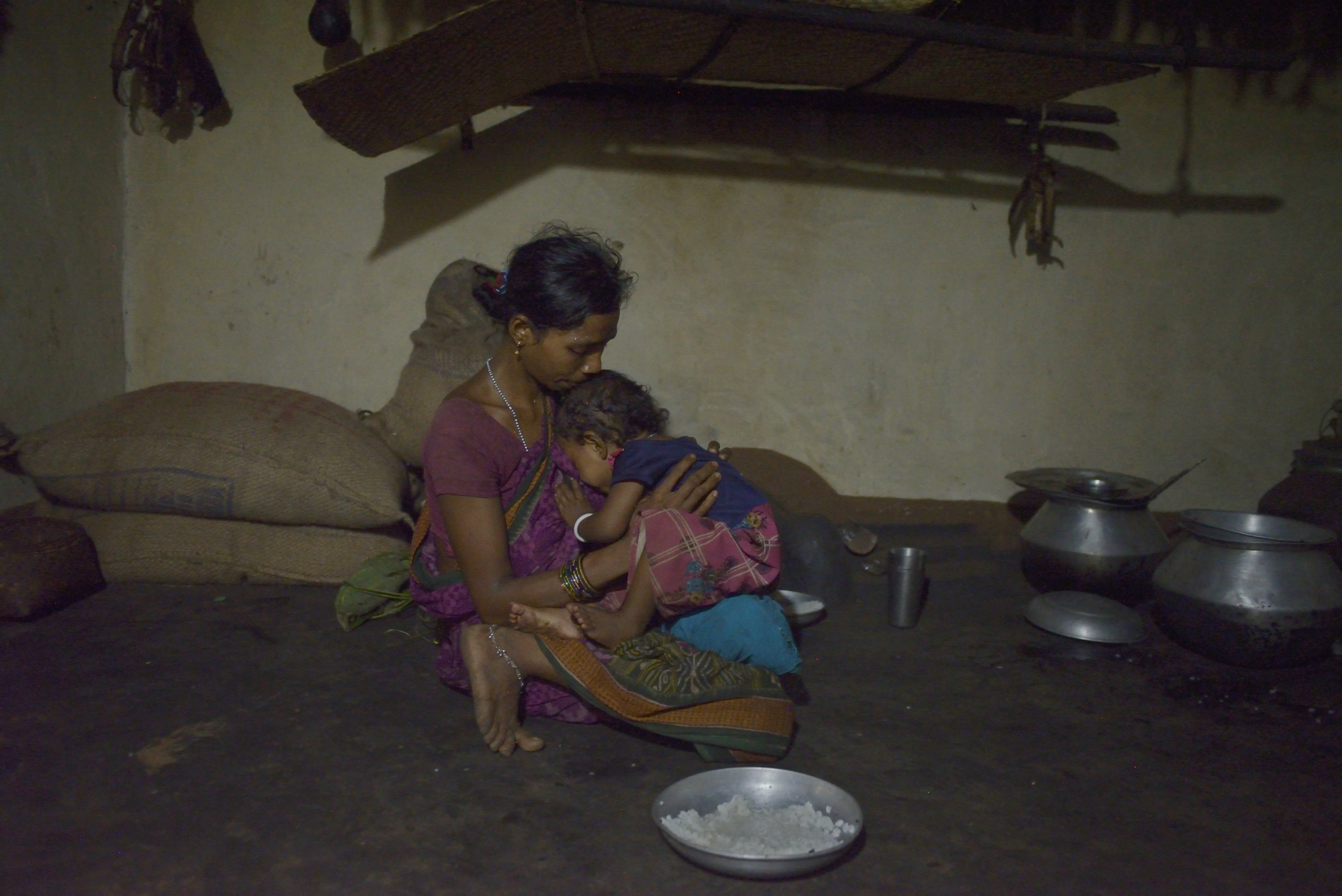 A woman and her daughter sitting next to some pots where they are preparing curries and rice