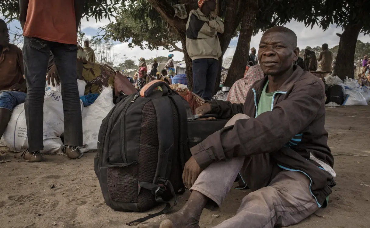 Man sitting on ground with backpack in crowded area.