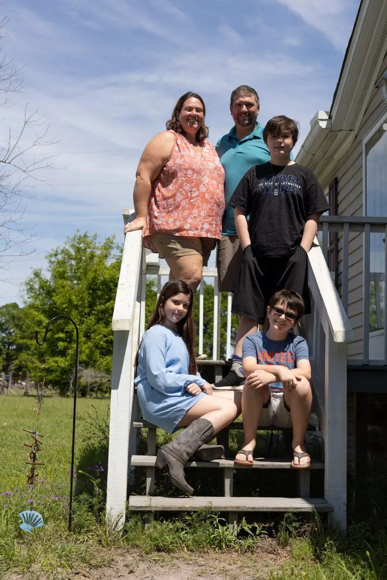 a family poses on the wooden stairs outside of their home.