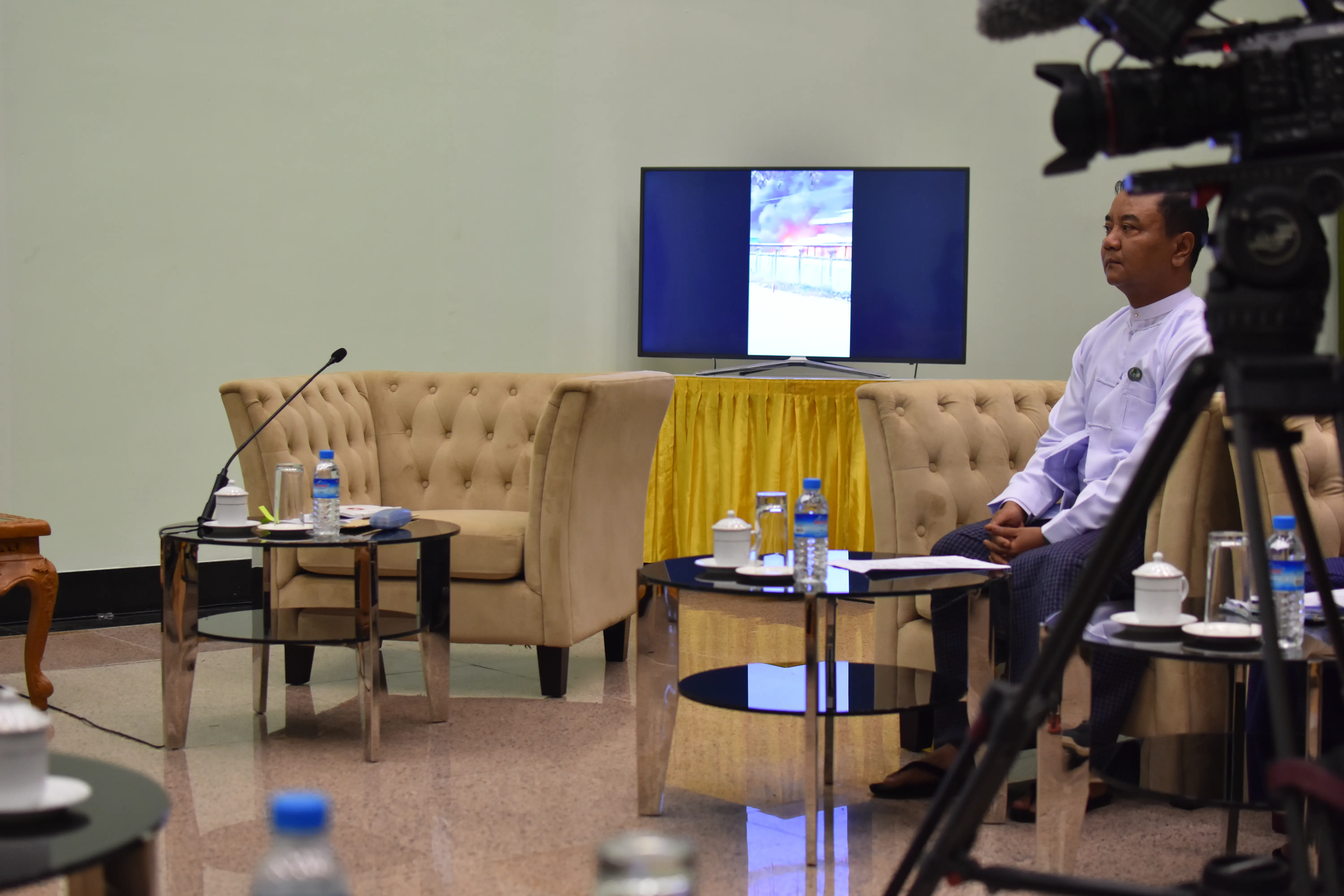 A person sits in a chair in a room with cameras and microphones.