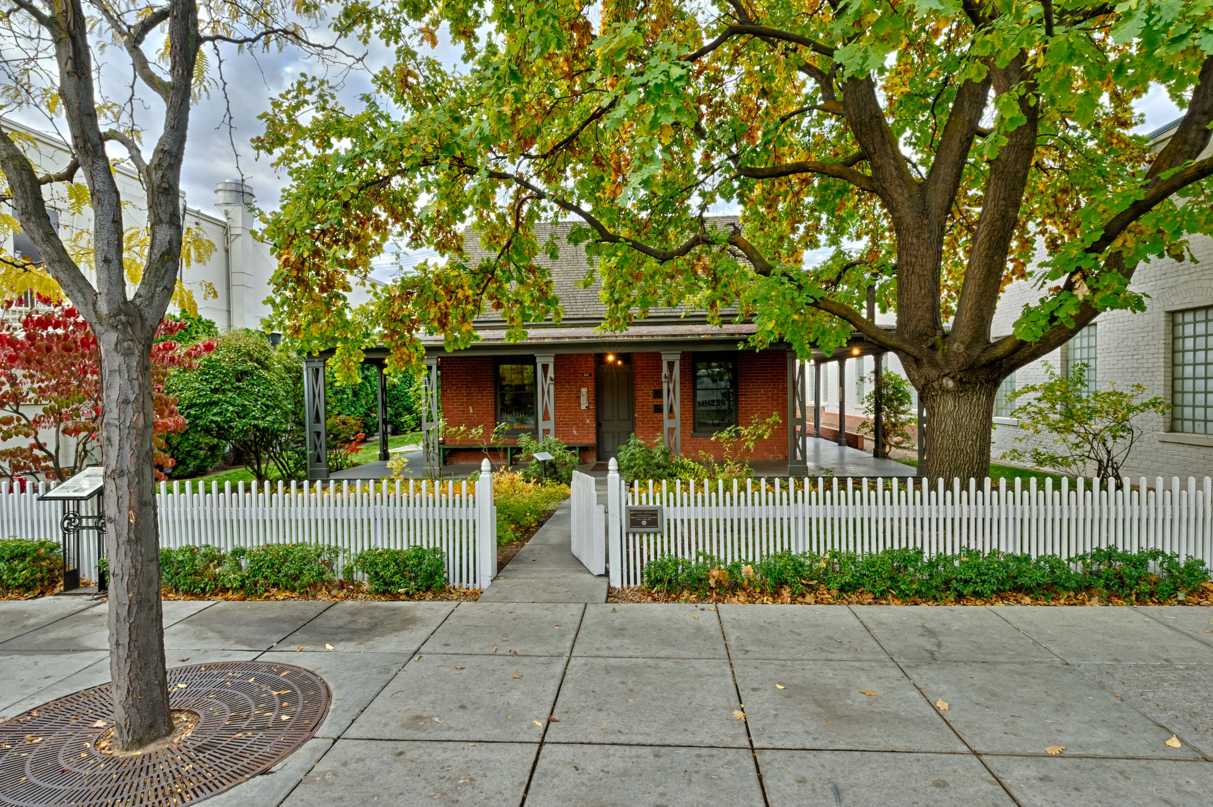 A brick building with trees and a white fence in front of it.